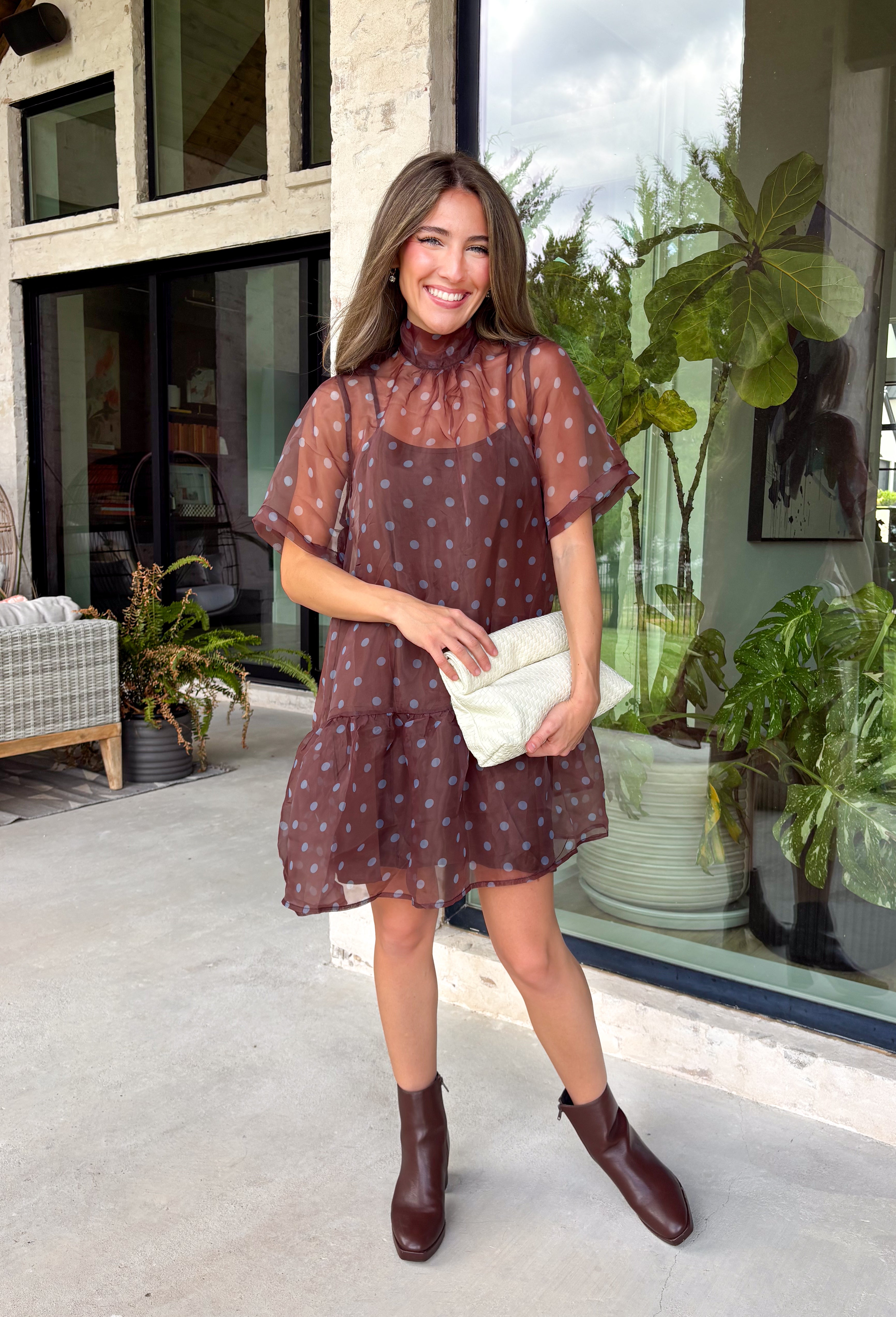 Classic polka dots get a fresh seasonal update in this charming dress from Entro. Designed with a rich brown backdrop and playful blue polka dots, this effortlessly feminine dress is perfect for everything from brunch dates to weekend outings. The high neckline creates a polished silhouette, while the back tie detail adds a sweet finishing touch. A flirty ruffle hem brings beautiful movement, and the fully lined lightweight fabric keeps you comfortable all day long.
