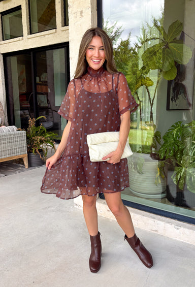 Classic polka dots get a fresh seasonal update in this charming dress from Entro. Designed with a rich brown backdrop and playful blue polka dots, this effortlessly feminine dress is perfect for everything from brunch dates to weekend outings. The high neckline creates a polished silhouette, while the back tie detail adds a sweet finishing touch. A flirty ruffle hem brings beautiful movement, and the fully lined lightweight fabric keeps you comfortable all day long.