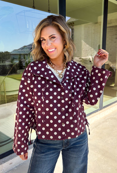 Give your fall layers a playful update with this wine-colored polka dot jacket from Entro. The rich wine shade is covered in classic white polka dots, creating a fun statement print that still pairs easily with your favorite seasonal neutrals. A collared neckline and button-down front give it a classic jacket feel, while tie details at the front and sides of the hem add a unique finishing touch. 