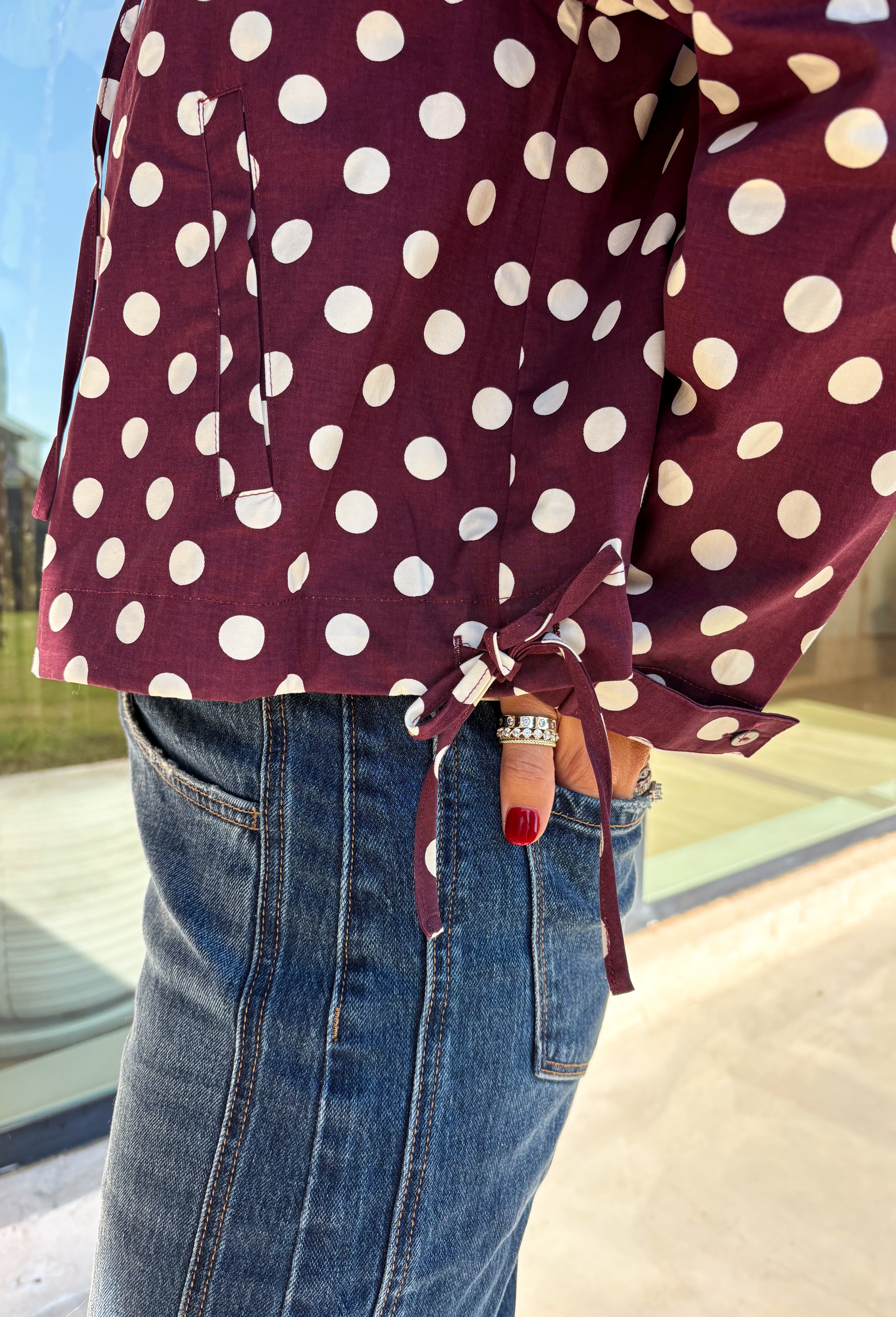 Give your fall layers a playful update with this wine-colored polka dot jacket from Entro. The rich wine shade is covered in classic white polka dots, creating a fun statement print that still pairs easily with your favorite seasonal neutrals. A collared neckline and button-down front give it a classic jacket feel, while tie details at the front and sides of the hem add a unique finishing touch. 