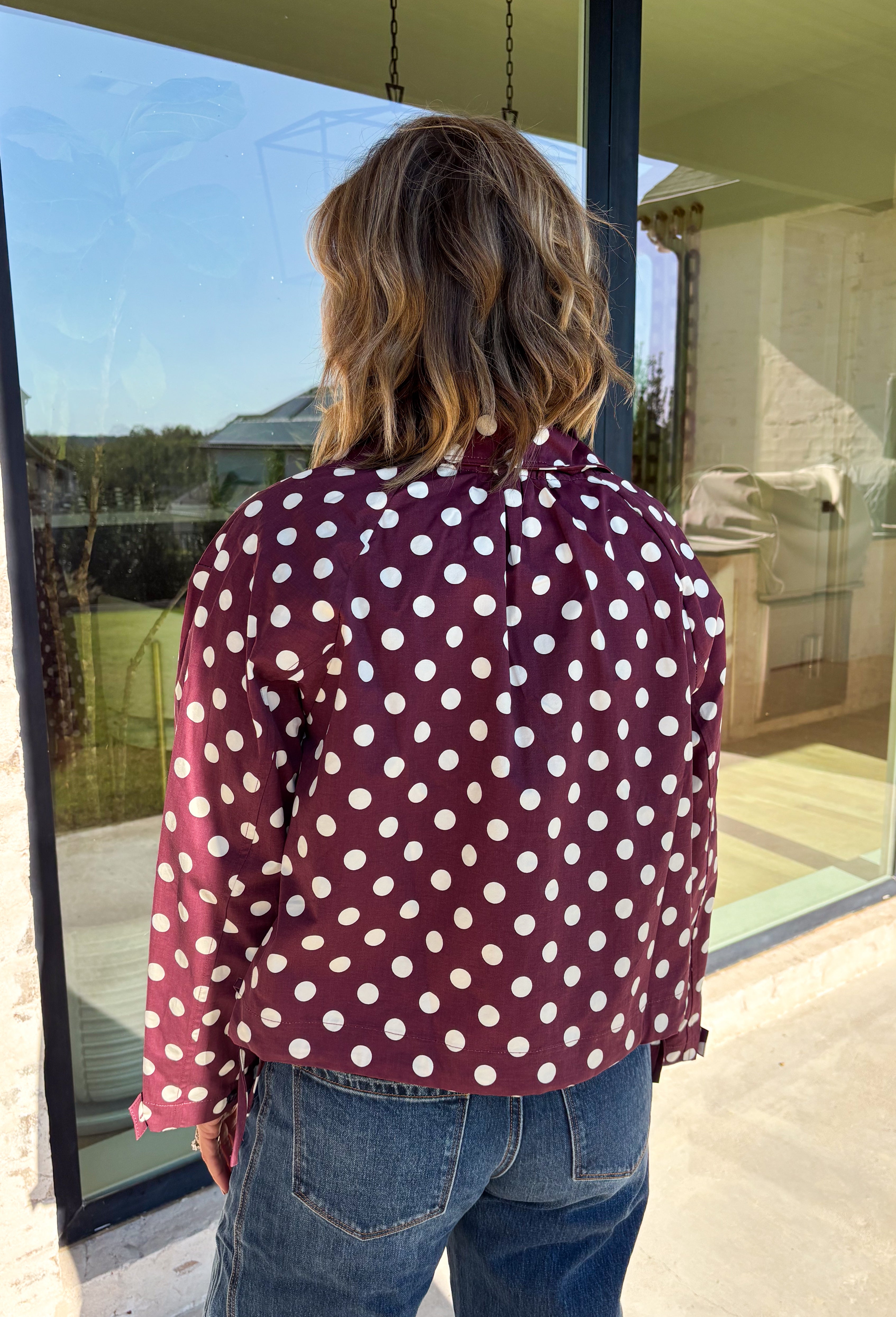 Give your fall layers a playful update with this wine-colored polka dot jacket from Entro. The rich wine shade is covered in classic white polka dots, creating a fun statement print that still pairs easily with your favorite seasonal neutrals. A collared neckline and button-down front give it a classic jacket feel, while tie details at the front and sides of the hem add a unique finishing touch. 