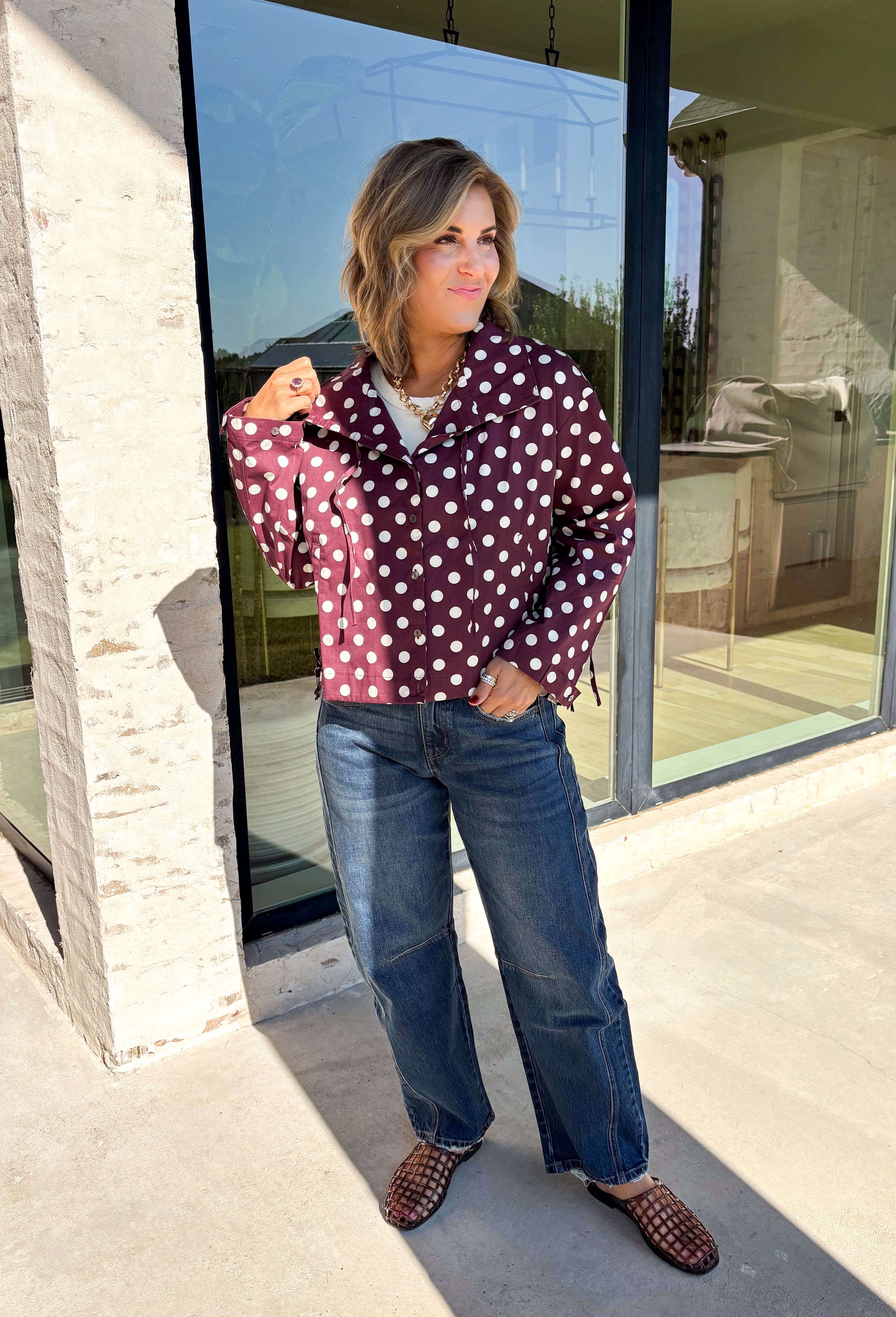 Give your fall layers a playful update with this wine-colored polka dot jacket from Entro. The rich wine shade is covered in classic white polka dots, creating a fun statement print that still pairs easily with your favorite seasonal neutrals. A collared neckline and button-down front give it a classic jacket feel, while tie details at the front and sides of the hem add a unique finishing touch. 