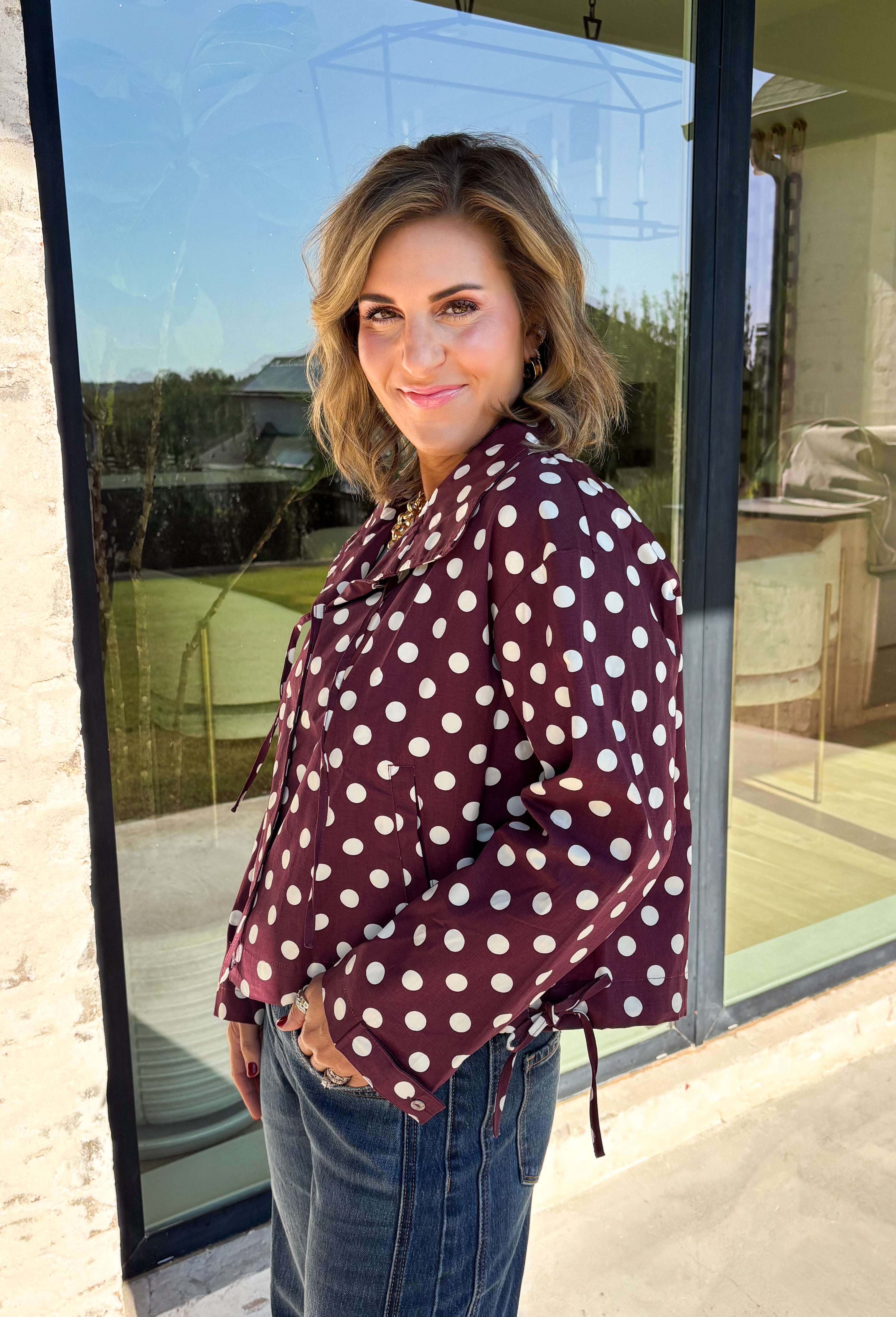 Give your fall layers a playful update with this wine-colored polka dot jacket from Entro. The rich wine shade is covered in classic white polka dots, creating a fun statement print that still pairs easily with your favorite seasonal neutrals. A collared neckline and button-down front give it a classic jacket feel, while tie details at the front and sides of the hem add a unique finishing touch. 