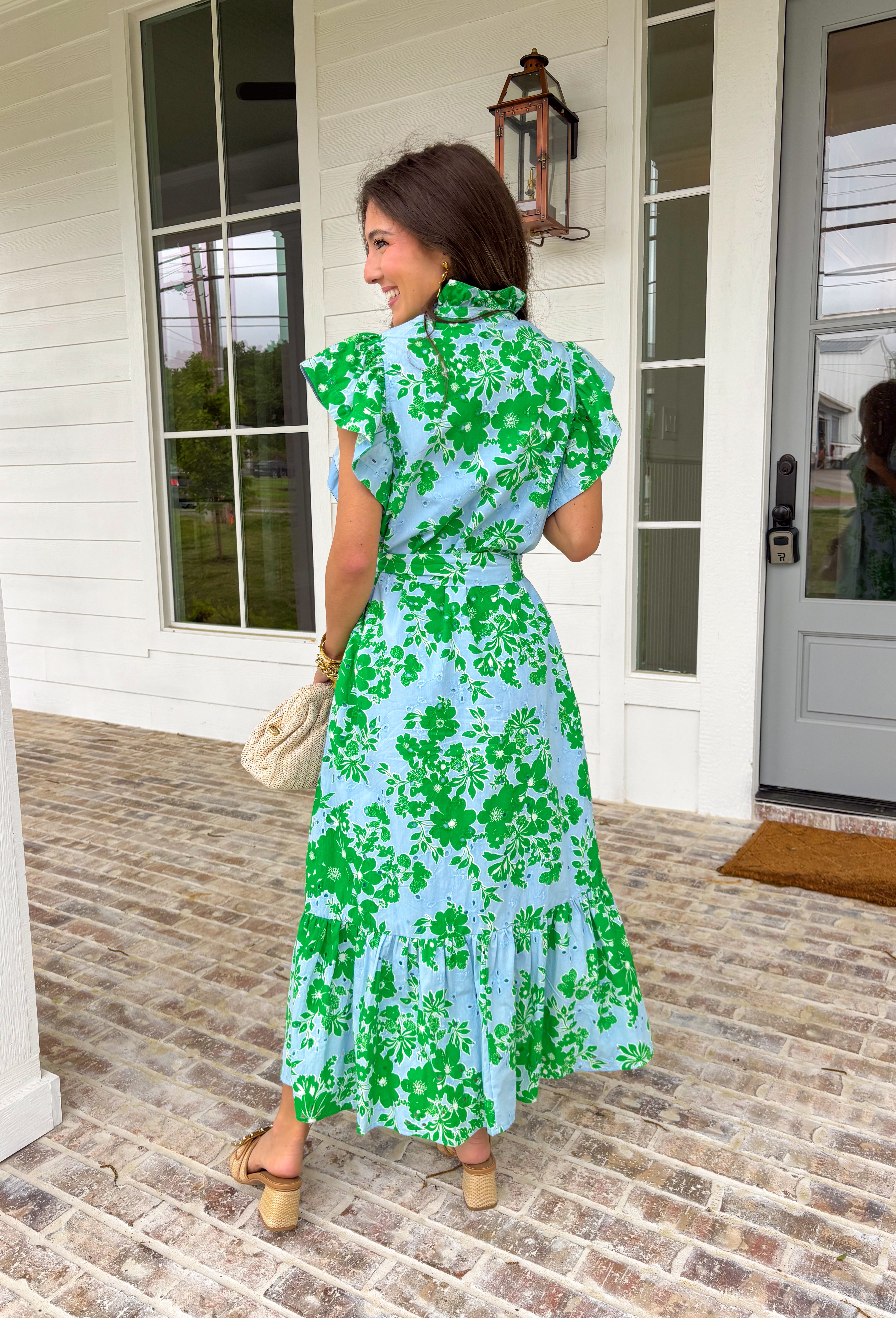 Soft, feminine, and full of spring charm! This light blue midi dress features delicate eyelet lace detailing throughout paired with a fresh green floral print for the prettiest layered texture. The subtle ruffle neckline adds a romantic touch, while the gold button details down the front bring a hint of shine. Designed with a matching self-tie closure to gently define the waist and a flowy tiered skirt for beautiful movement, this dress feels both polished and easy to wear. 