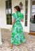 Soft, feminine, and full of spring charm! This light blue midi dress features delicate eyelet lace detailing throughout paired with a fresh green floral print for the prettiest layered texture. The subtle ruffle neckline adds a romantic touch, while the gold button details down the front bring a hint of shine. Designed with a matching self-tie closure to gently define the waist and a flowy tiered skirt for beautiful movement, this dress feels both polished and easy to wear. 