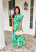 Soft, feminine, and full of spring charm! This light blue midi dress features delicate eyelet lace detailing throughout paired with a fresh green floral print for the prettiest layered texture. The subtle ruffle neckline adds a romantic touch, while the gold button details down the front bring a hint of shine. Designed with a matching self-tie closure to gently define the waist and a flowy tiered skirt for beautiful movement, this dress feels both polished and easy to wear. 