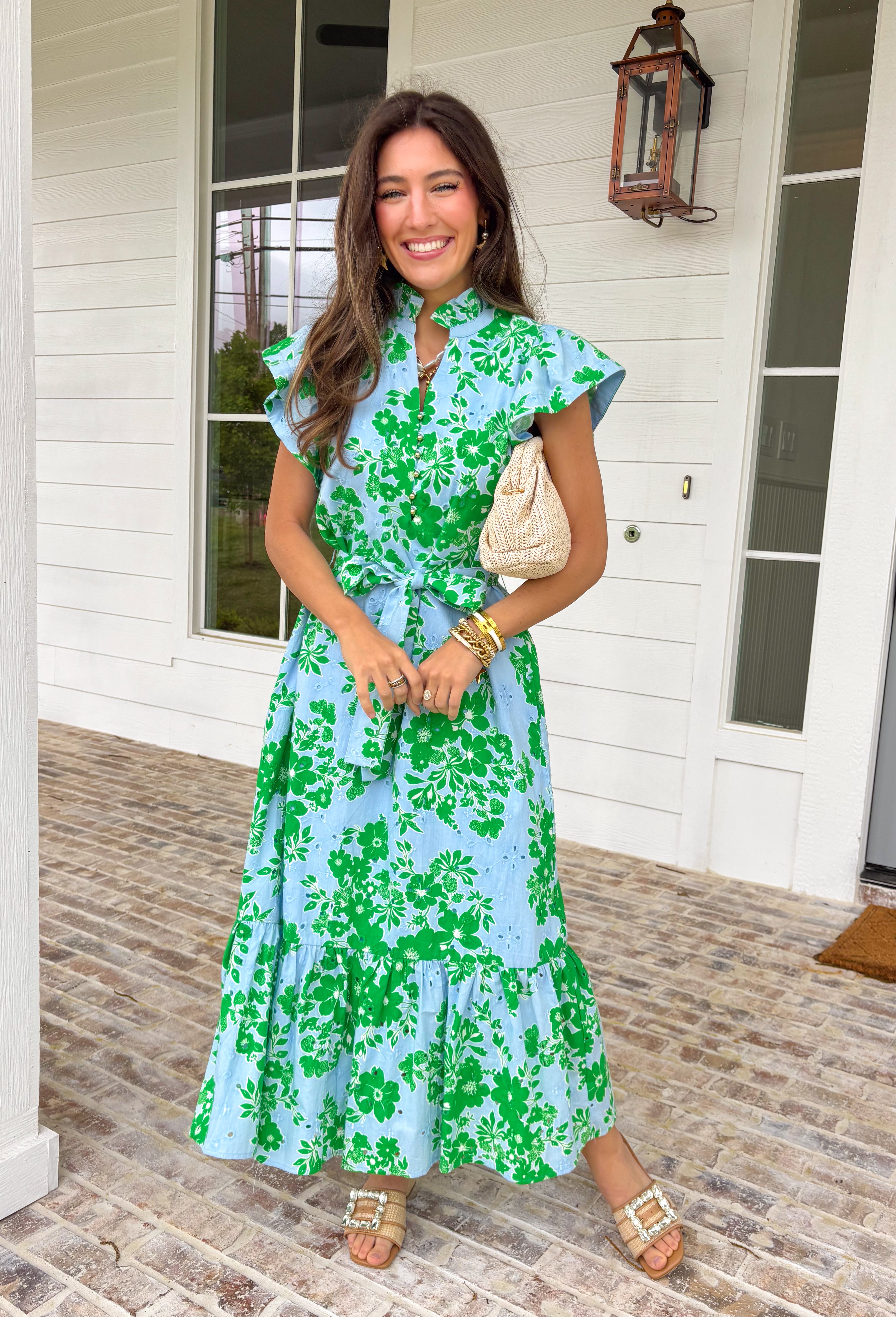 Soft, feminine, and full of spring charm! This light blue midi dress features delicate eyelet lace detailing throughout paired with a fresh green floral print for the prettiest layered texture. The subtle ruffle neckline adds a romantic touch, while the gold button details down the front bring a hint of shine. Designed with a matching self-tie closure to gently define the waist and a flowy tiered skirt for beautiful movement, this dress feels both polished and easy to wear. 