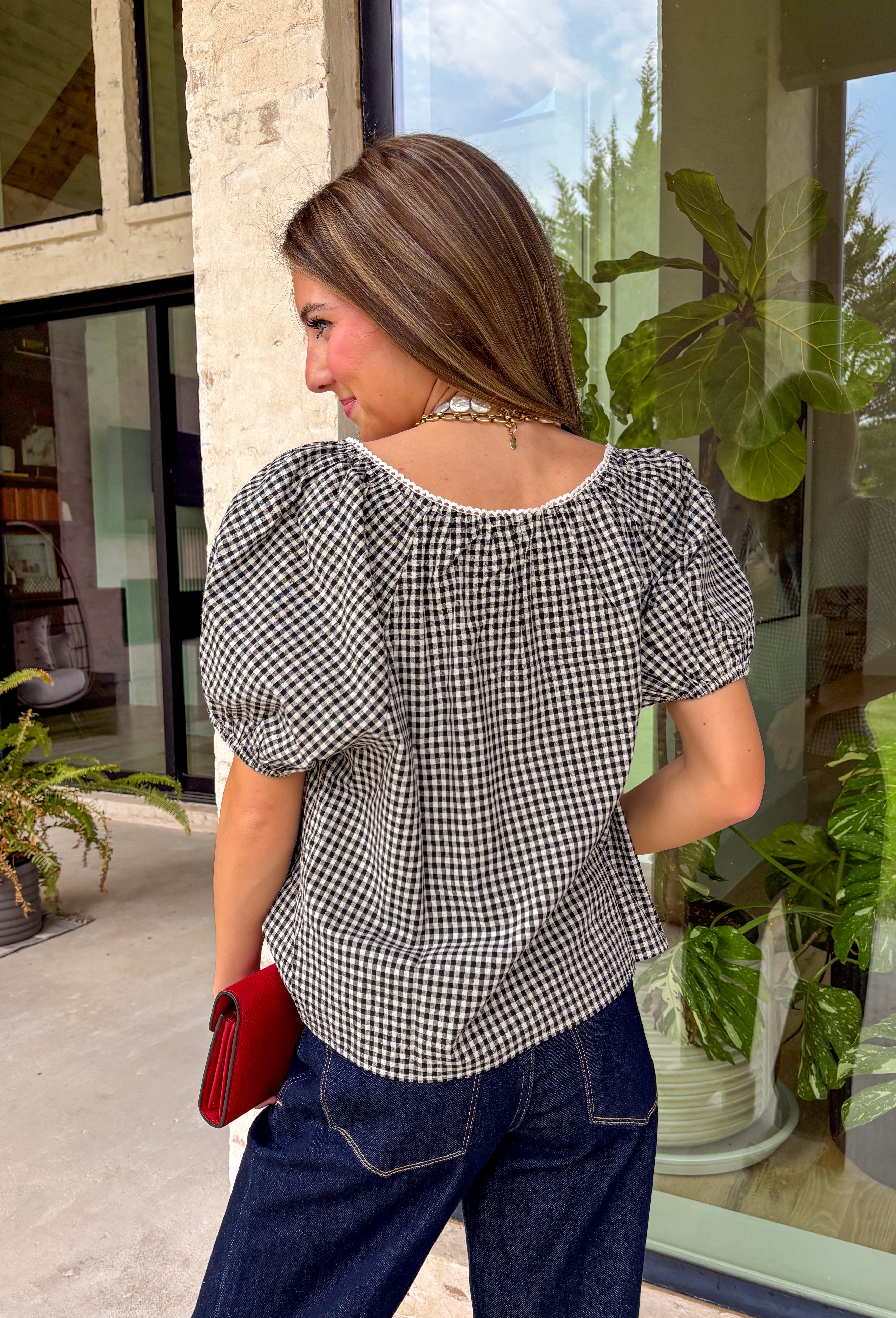 A timeless gingham print gets a feminine update in this charming button-down blouse from Twentifourth. Featuring a classic black and white gingham pattern, this versatile top is accented with delicate white scallop trim across the front for an extra touch of sweetness. The short sleeves are finished with comfortable elastic cuffs that create a soft puff silhouette, while the button-front design and breathable cotton blend make it an easy favorite for everyday wear. 
