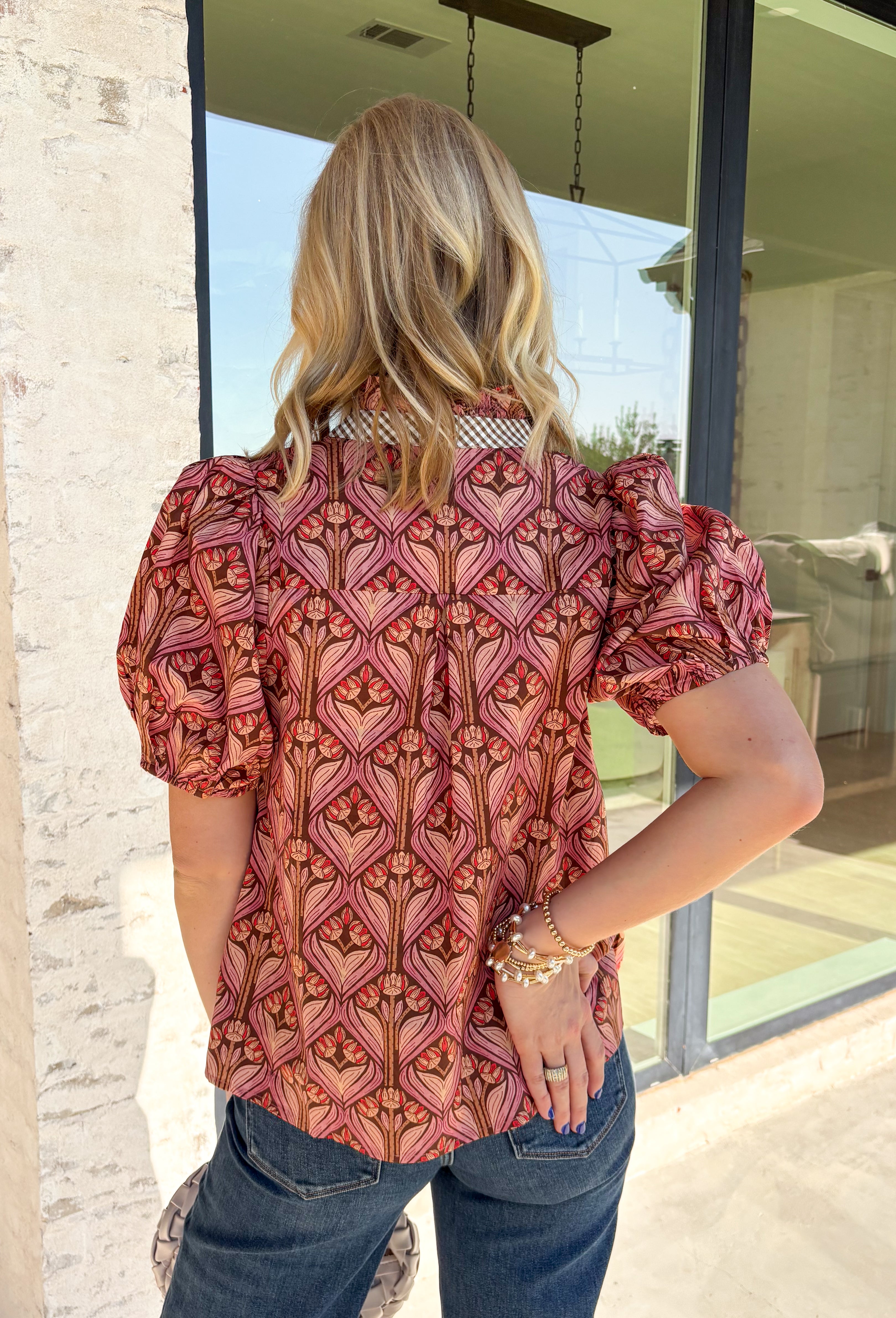 Add a touch of feminine charm to your everyday wardrobe with this beautifully detailed top from Entro. Featuring a rich brown backdrop with a pink floral print, this timeless blouse is full of thoughtful details you'll love. The ruffled neckline creates an effortlessly polished look, while the brown gingham contrast trim adds the perfect pop of classic charm. 