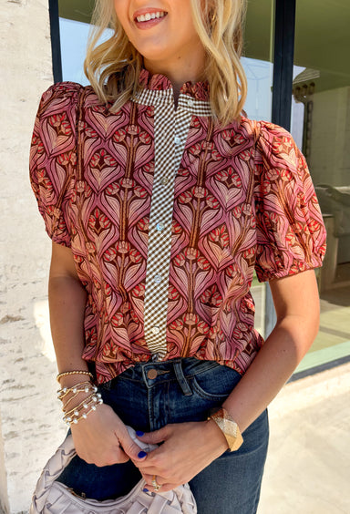 Add a touch of feminine charm to your everyday wardrobe with this beautifully detailed top from Entro. Featuring a rich brown backdrop with a pink floral print, this timeless blouse is full of thoughtful details you'll love. The ruffled neckline creates an effortlessly polished look, while the brown gingham contrast trim adds the perfect pop of classic charm. 
