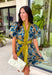 Bring timeless charm to your fall wardrobe with this beautifully detailed floral dress. Designed in a rich olive green with a stunning blue and navy floral print, this cotton dress is the perfect blend of classic and feminine. The flattering v-neckline, button-front design, and self-tie waist create a silhouette that's effortlessly polished, while the gathered back yoke adds a soft, flowy fit you'll love.