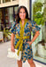 Bring timeless charm to your fall wardrobe with this beautifully detailed floral dress. Designed in a rich olive green with a stunning blue and navy floral print, this cotton dress is the perfect blend of classic and feminine. The flattering v-neckline, button-front design, and self-tie waist create a silhouette that's effortlessly polished, while the gathered back yoke adds a soft, flowy fit you'll love.