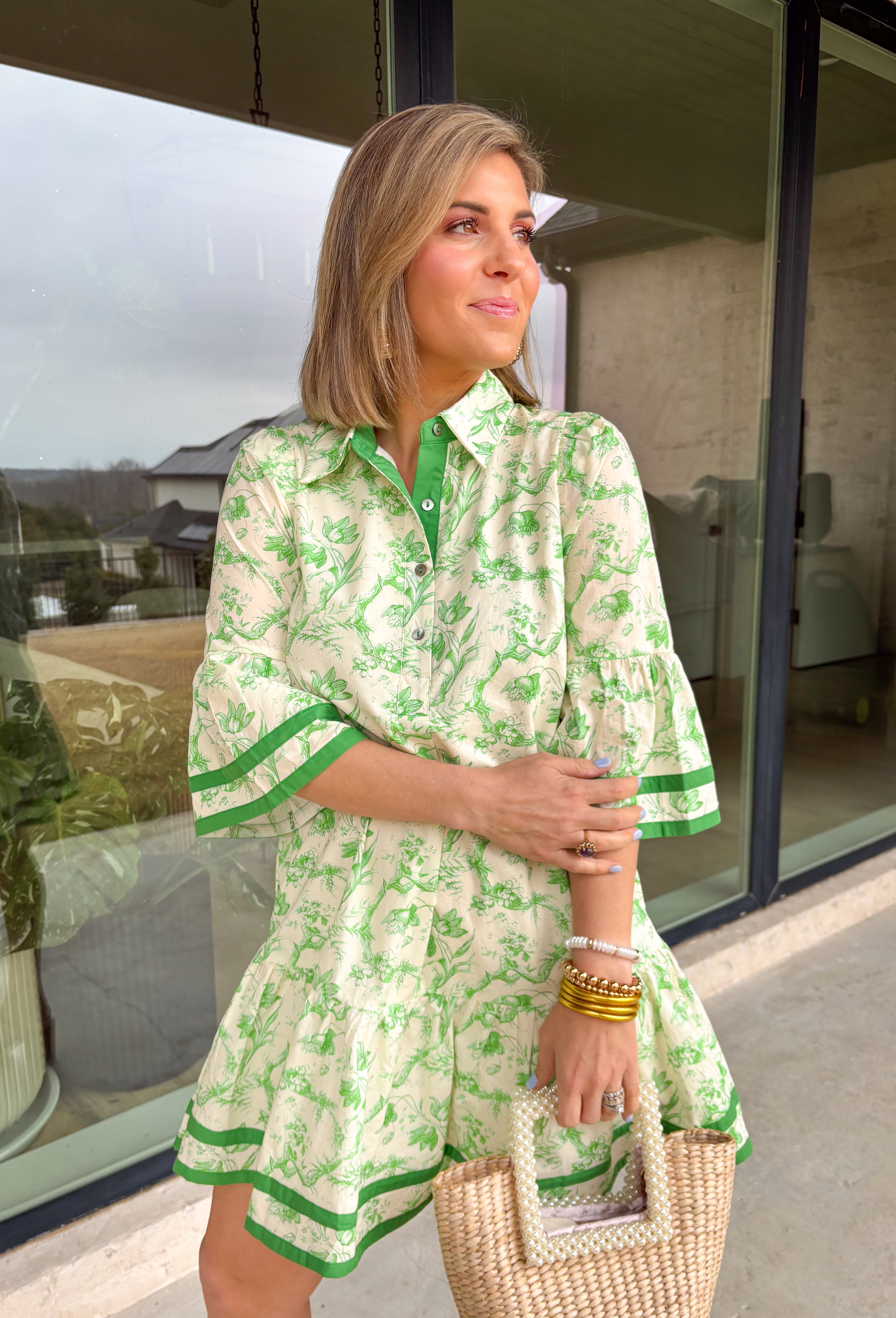 Fresh, timeless, and perfect for spring, this off-white dress by Entro is an easy favorite for sunny days ahead. Featuring a light green floral print throughout, it has a soft, feminine look that feels effortlessly wearable. Dark green trim along the sleeves and hem adds a polished contrast, while the front button details give it a classic touch. Finished with side pockets and a full lining, this dress is comfortable, flattering, and ready for everything from brunch to spring events.