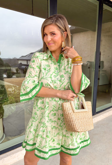 Fresh, timeless, and perfect for spring, this off-white dress by Entro is an easy favorite for sunny days ahead. Featuring a light green floral print throughout, it has a soft, feminine look that feels effortlessly wearable. Dark green trim along the sleeves and hem adds a polished contrast, while the front button details give it a classic touch. Finished with side pockets and a full lining, this dress is comfortable, flattering, and ready for everything from brunch to spring events.