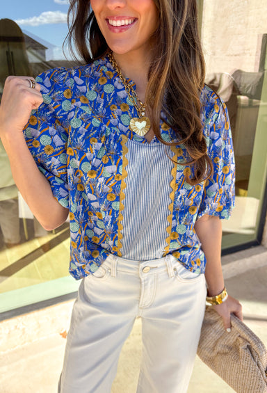 Sweet, colorful, and full of spring charm, this blue short sleeve top by Voy is a total standout. Featuring a soft floral print in shades of blue, sage, and mustard, it brings the prettiest pop of color to your everyday look. Blue and white striped detailing down the front (and a matching stripe accent on the back!) adds a fun contrast, while mustard ricrack trim gives it the cutest vintage-inspired touch. Finished with elastic puff sleeves for a feminine silhouette, this top is an easy way to dress up your