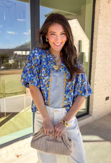 Sweet, colorful, and full of spring charm, this blue short sleeve top by Voy is a total standout. Featuring a soft floral print in shades of blue, sage, and mustard, it brings the prettiest pop of color to your everyday look. Blue and white striped detailing down the front (and a matching stripe accent on the back!) adds a fun contrast, while mustard ricrack trim gives it the cutest vintage-inspired touch. Finished with elastic puff sleeves for a feminine silhouette, this top is an easy way to dress up your