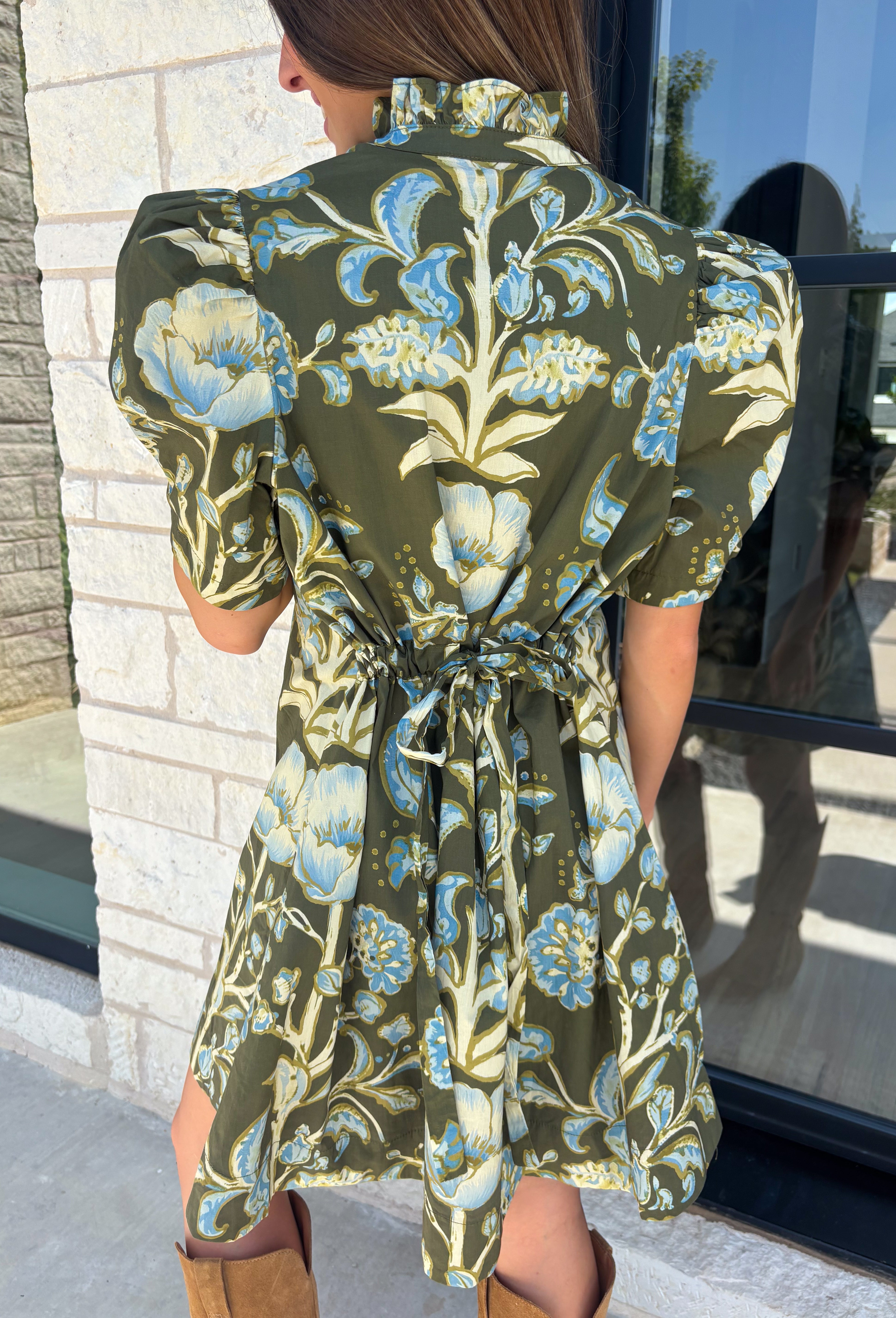 Welcome the season in effortless style with this charming floral dress! Featuring a rich olive backdrop with beautiful blue and soft green florals, this dress captures everything we love about fall. The ruffled high neckline and button front add timeless charm, while the self-tie waist in the back creates a flattering silhouette that's easy to customize. Finished with short puff sleeves, side pockets, and a fully lined design.