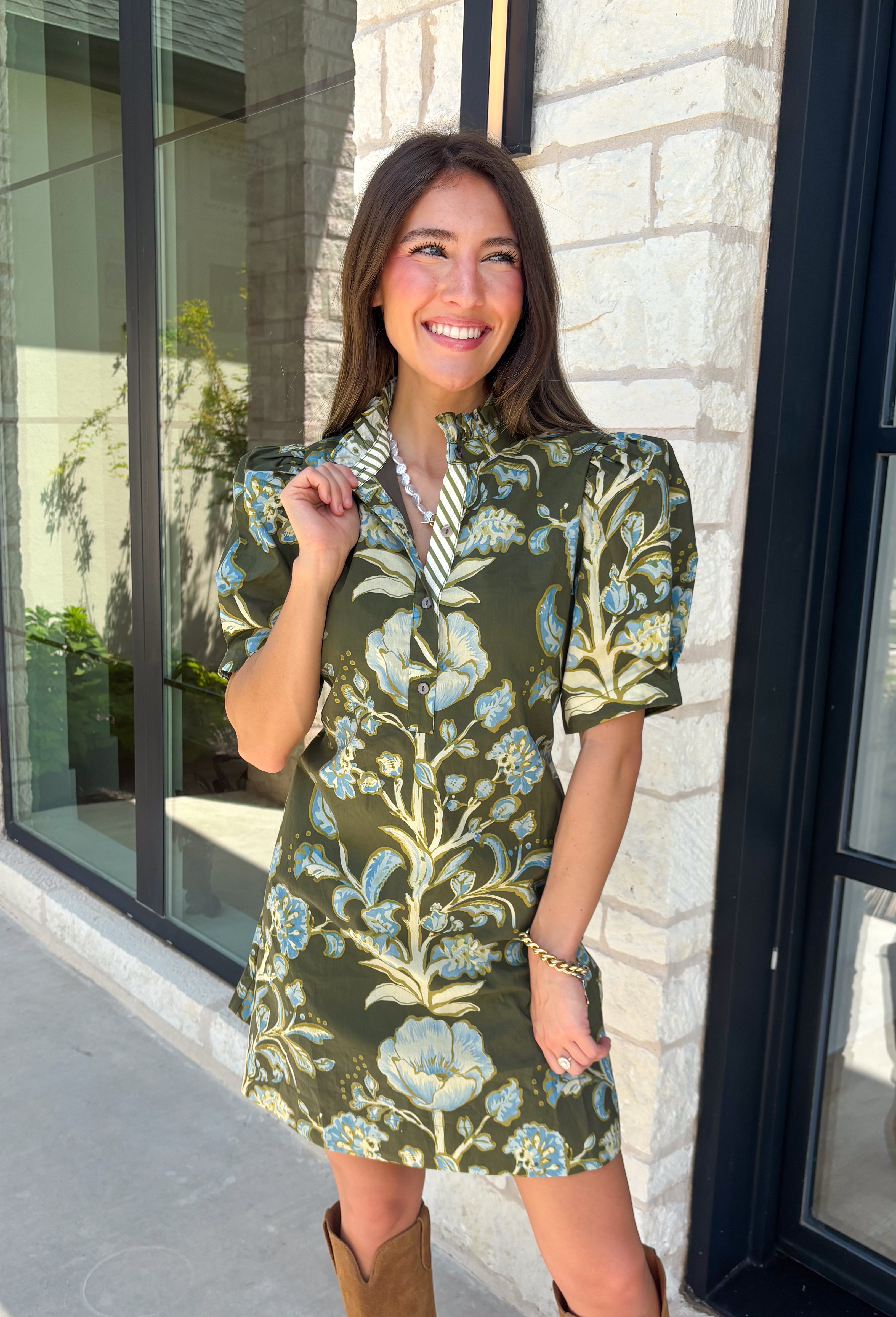 Welcome the season in effortless style with this charming floral dress! Featuring a rich olive backdrop with beautiful blue and soft green florals, this dress captures everything we love about fall. The ruffled high neckline and button front add timeless charm, while the self-tie waist in the back creates a flattering silhouette that's easy to customize. Finished with short puff sleeves, side pockets, and a fully lined design.