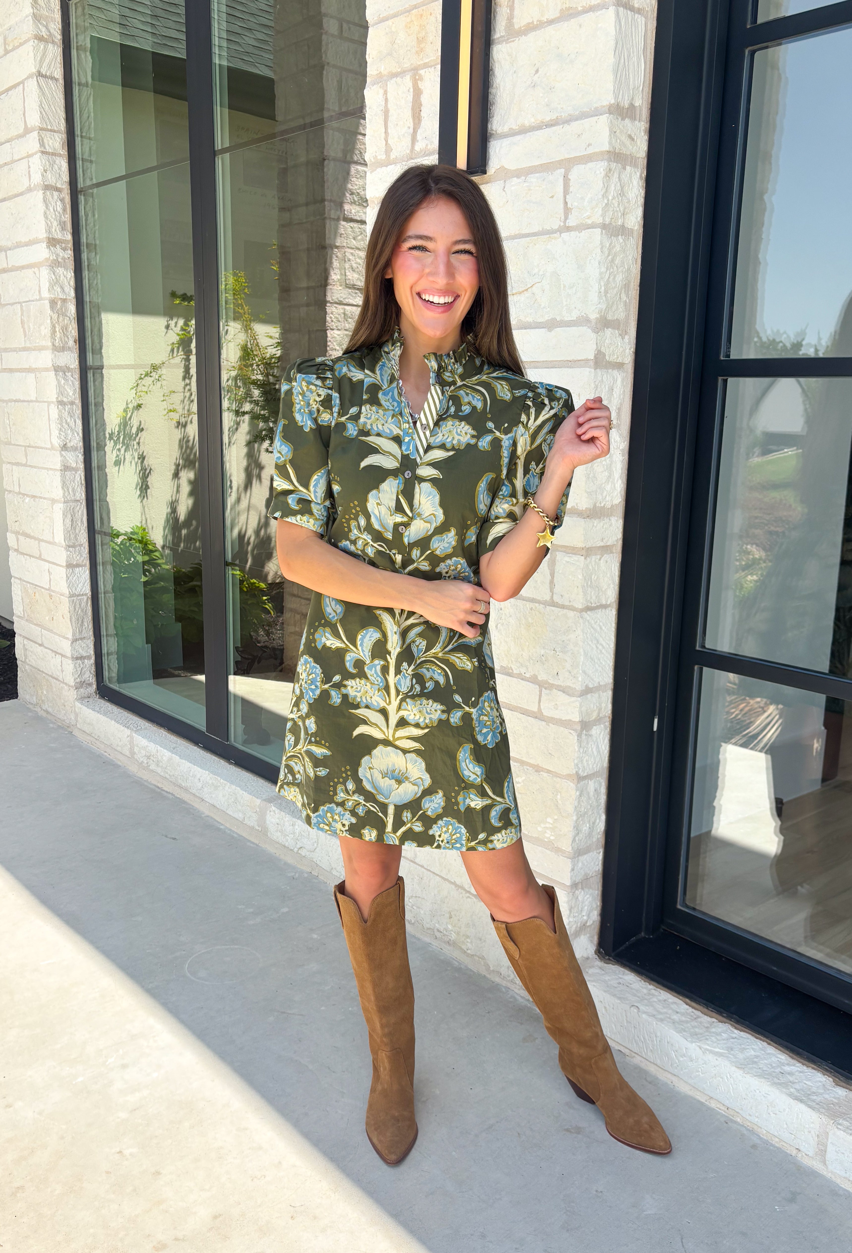 Welcome the season in effortless style with this charming floral dress! Featuring a rich olive backdrop with beautiful blue and soft green florals, this dress captures everything we love about fall. The ruffled high neckline and button front add timeless charm, while the self-tie waist in the back creates a flattering silhouette that's easy to customize. Finished with short puff sleeves, side pockets, and a fully lined design.