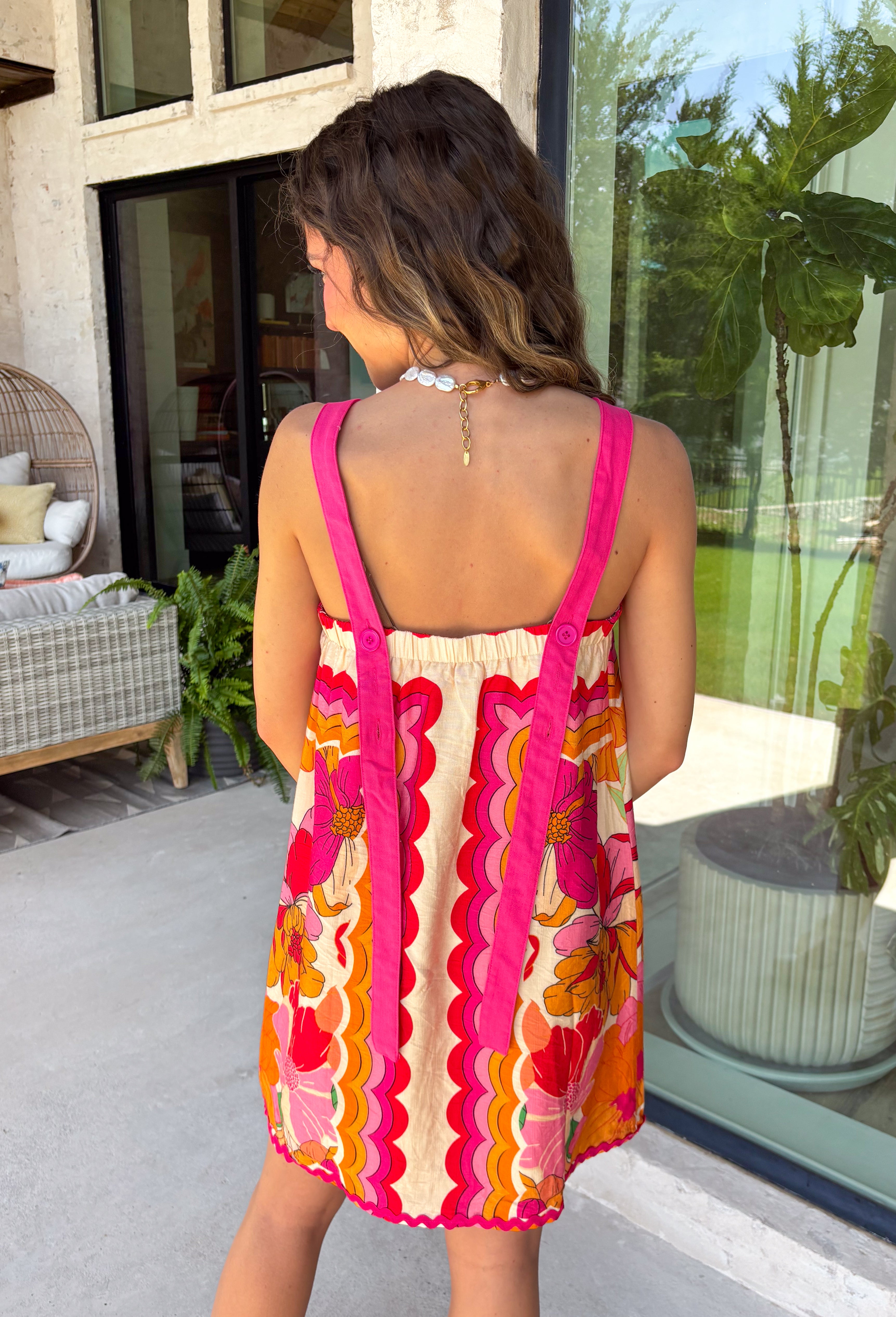 Bring on the sunshine in this vibrant floral dress! Designed with a neutral backdrop and a bold abstract floral print in shades of red, orange, pink, with pops of green and black, this dress is made to stand out all summer long. The pink rickrack trim along the front and hem adds a playful, vintage-inspired touch, while the adjustable straps and elastic back create a comfortable, flattering fit. 