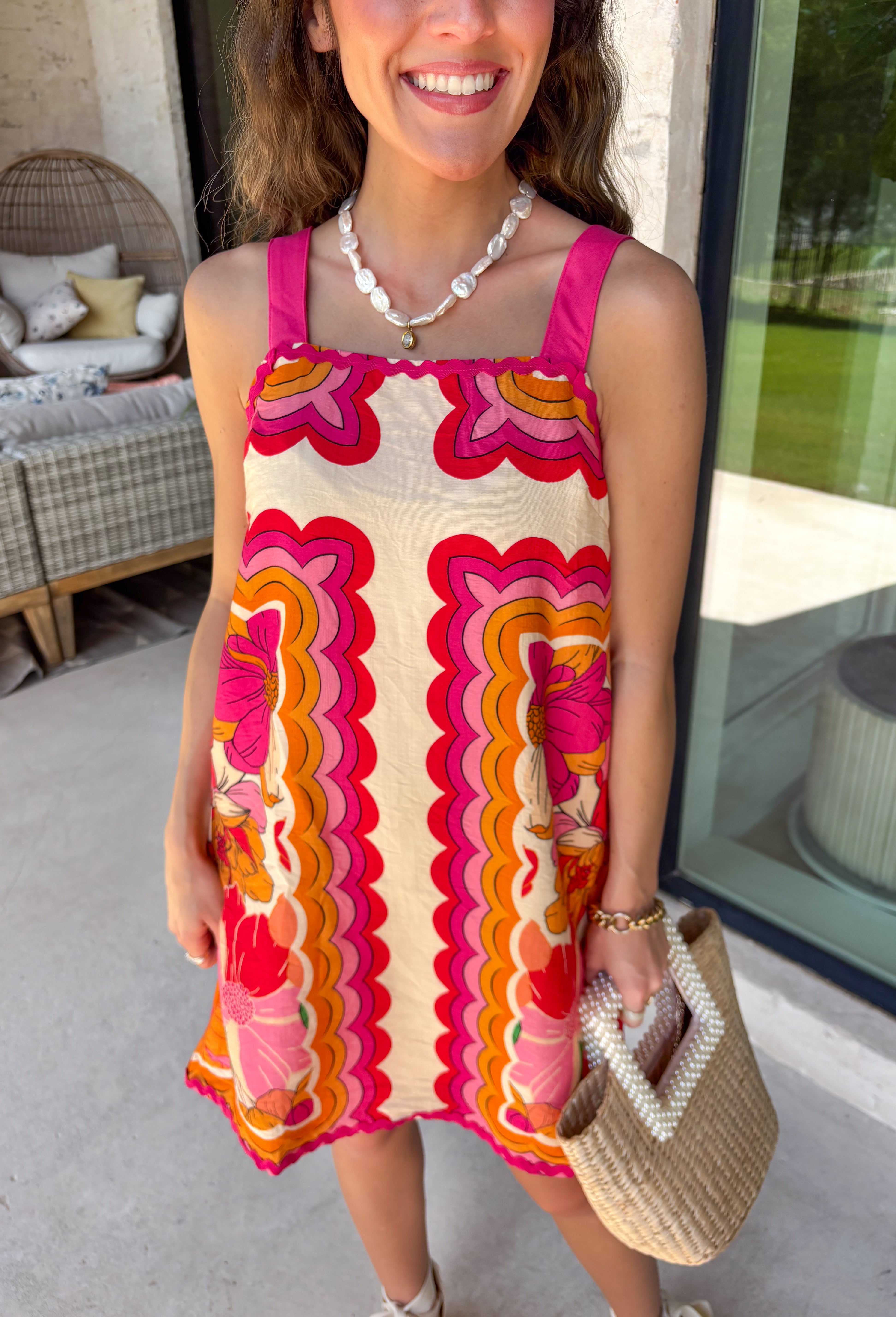 Bring on the sunshine in this vibrant floral dress! Designed with a neutral backdrop and a bold abstract floral print in shades of red, orange, pink, with pops of green and black, this dress is made to stand out all summer long. The pink rickrack trim along the front and hem adds a playful, vintage-inspired touch, while the adjustable straps and elastic back create a comfortable, flattering fit. 