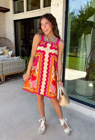 Bring on the sunshine in this vibrant floral dress! Designed with a neutral backdrop and a bold abstract floral print in shades of red, orange, pink, with pops of green and black, this dress is made to stand out all summer long. The pink rickrack trim along the front and hem adds a playful, vintage-inspired touch, while the adjustable straps and elastic back create a comfortable, flattering fit. 