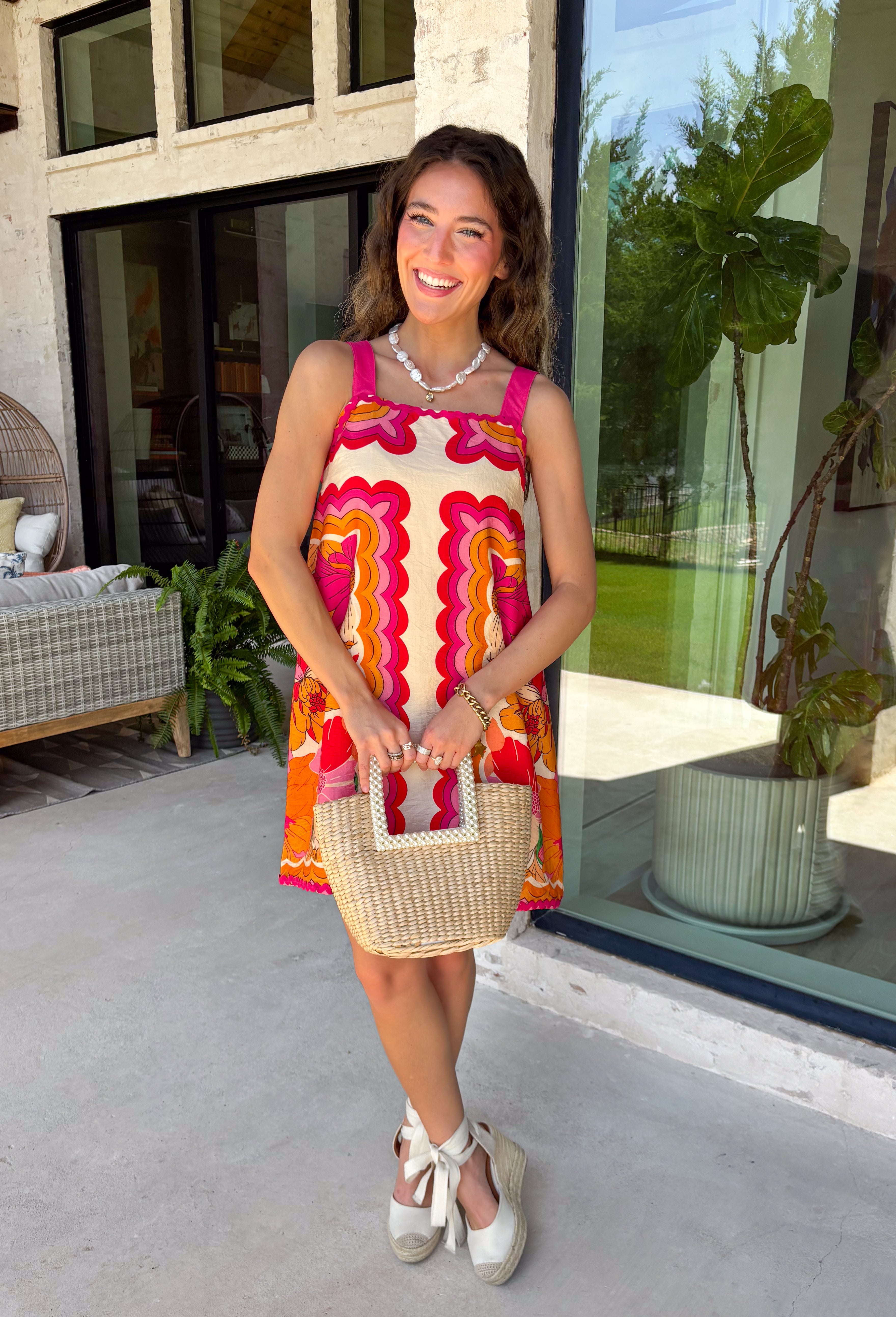 Bring on the sunshine in this vibrant floral dress! Designed with a neutral backdrop and a bold abstract floral print in shades of red, orange, pink, with pops of green and black, this dress is made to stand out all summer long. The pink rickrack trim along the front and hem adds a playful, vintage-inspired touch, while the adjustable straps and elastic back create a comfortable, flattering fit. 