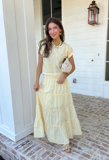This yellow and white stripe two piece set is bringing all the sunshine to your warm weather wardrobe! The short sleeve top features cuffed sleeves and a subtle keyhole closure for a polished touch, while the matching tiered midi skirt with an elastic waistband keeps things comfortable and flattering. Made from breathable 100% cotton, this set is perfect for warm days filled with brunch plans, baby showers, or weekend outings. 