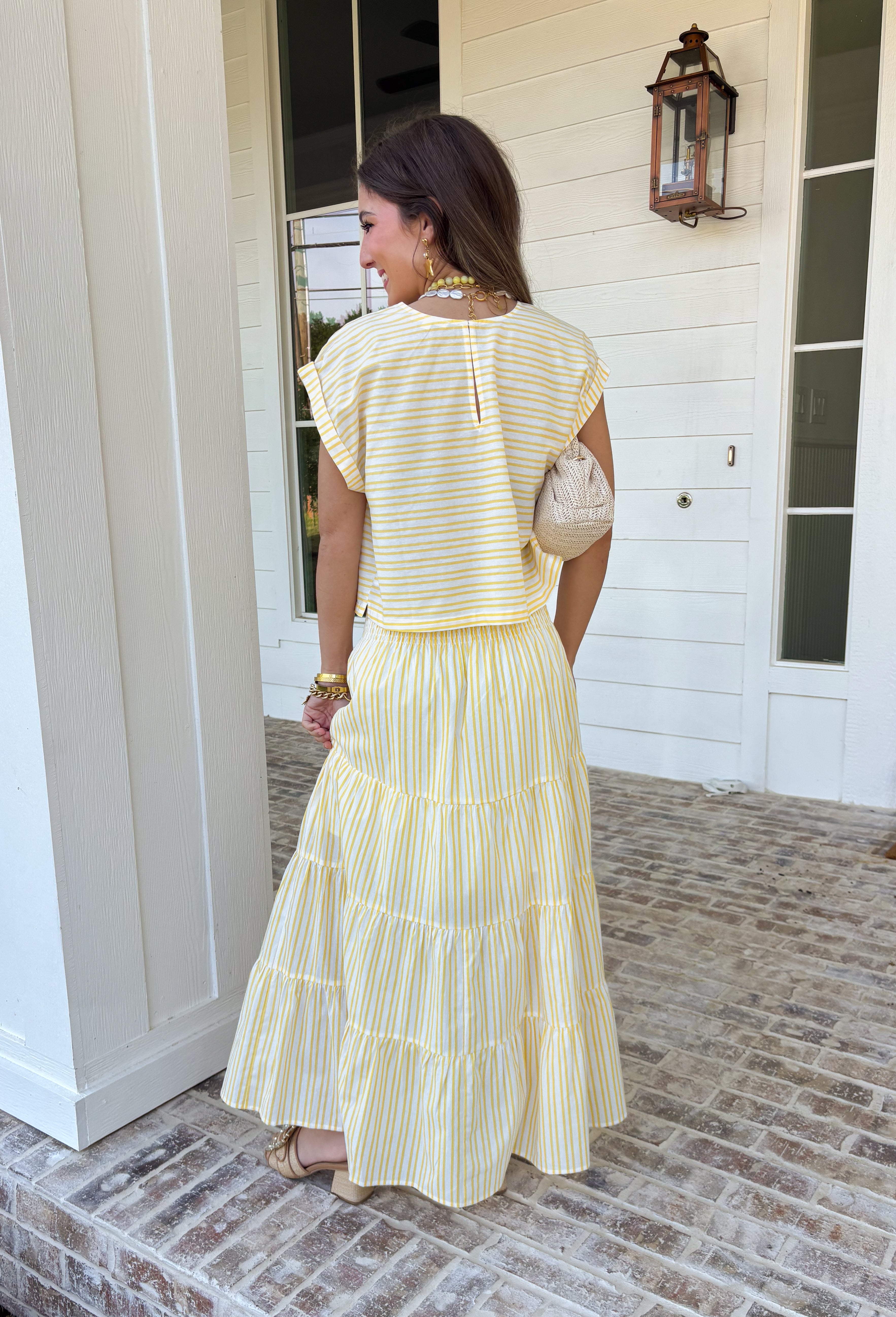 This yellow and white stripe two piece set is bringing all the sunshine to your warm weather wardrobe! The short sleeve top features cuffed sleeves and a subtle keyhole closure for a polished touch, while the matching tiered midi skirt with an elastic waistband keeps things comfortable and flattering. Made from breathable 100% cotton, this set is perfect for warm days filled with brunch plans, baby showers, or weekend outings. 