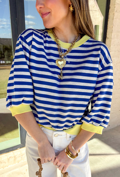 Bright, cheerful, and perfect for spring layering, this blue and off-white striped top by Entro adds a fun pop of color to a classic silhouette. Designed with 3/4 length sleeves, it features sunny yellow accents along the neckline, sleeve cuffs, and hem for a playful contrast that feels fresh and seasonal. Soft and lightweight, this top is easy to wear from casual days to weekend plans.