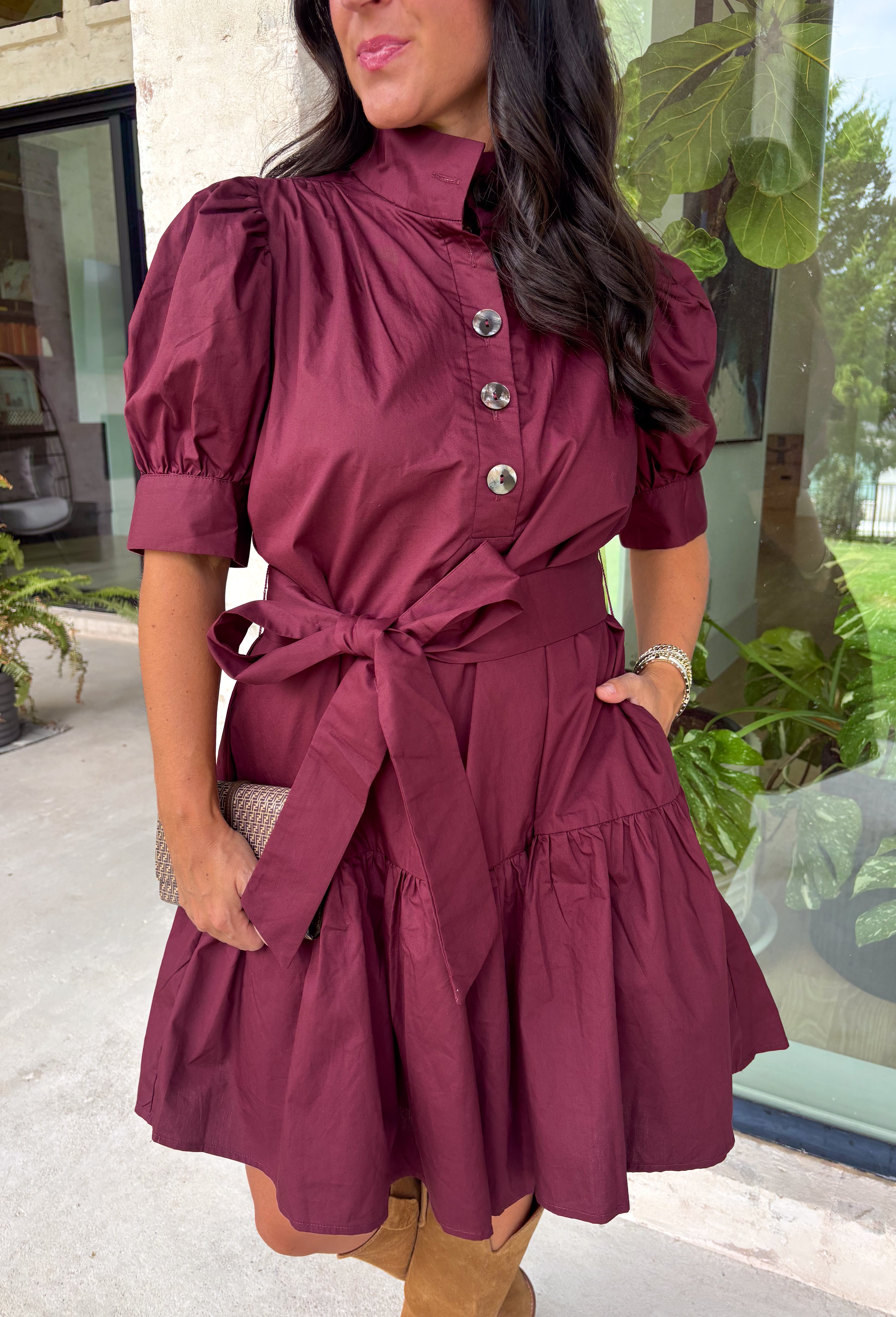 Rich in color and timeless in style, this burgundy dress is the perfect piece to carry you through the fall season. Designed with a classic button-front silhouette, this effortlessly feminine dress features charming puff sleeves and a matching self-tie belt that cinches the waist for a flattering, customizable fit. Side pockets add everyday functionality, while the fully lined cotton fabric keeps you comfortable from morning to night. 
