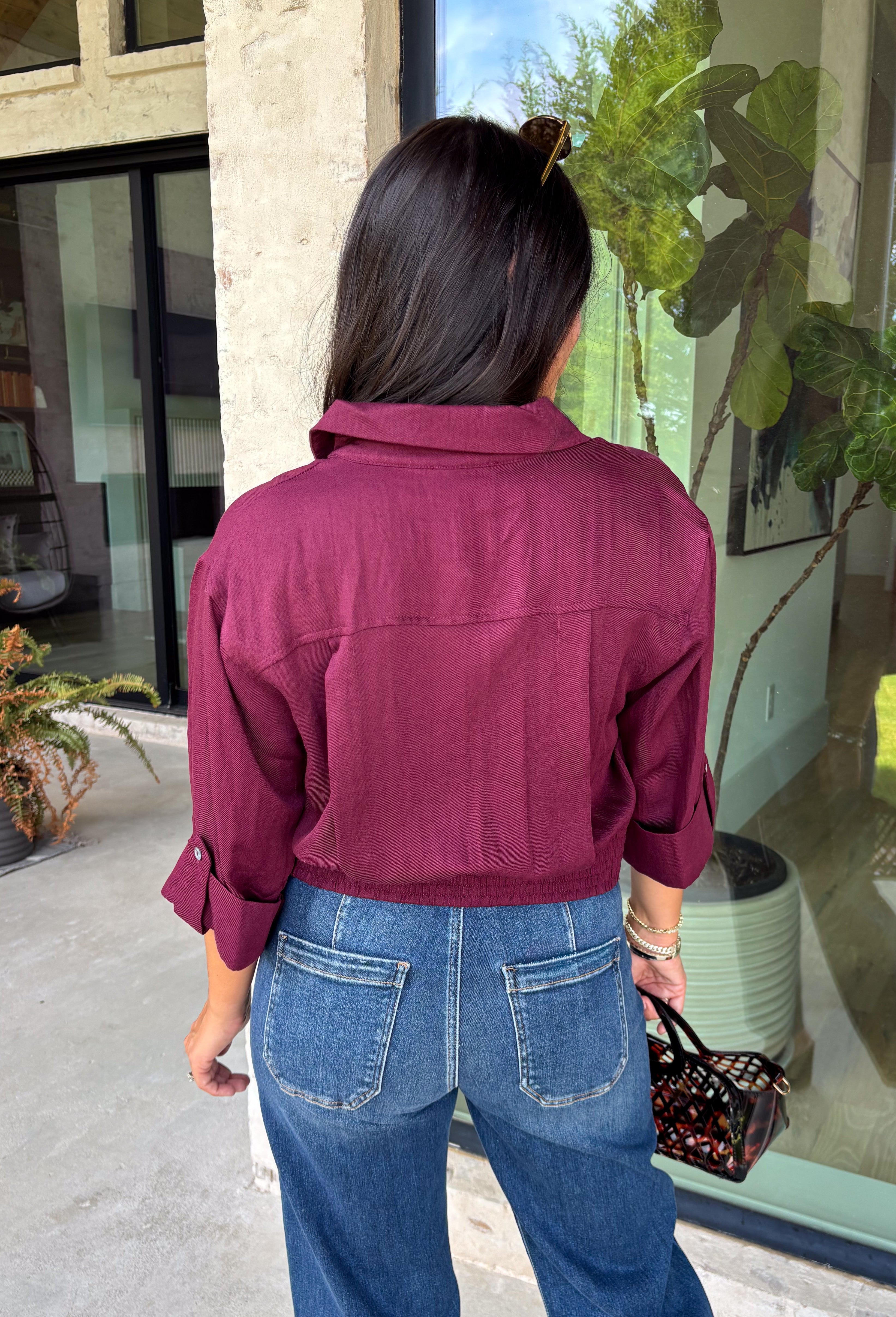 Every wardrobe needs a timeless wine blouse, and this versatile top from Entro is one you'll reach for again and again. Designed with a flattering v-neckline and button-front closure, this effortlessly polished piece transitions seamlessly from workdays to weekends. The ¾ roll-tab sleeves offer versatile styling, while the elasticized smocked back hem creates a comfortable fit with a modern touch. 