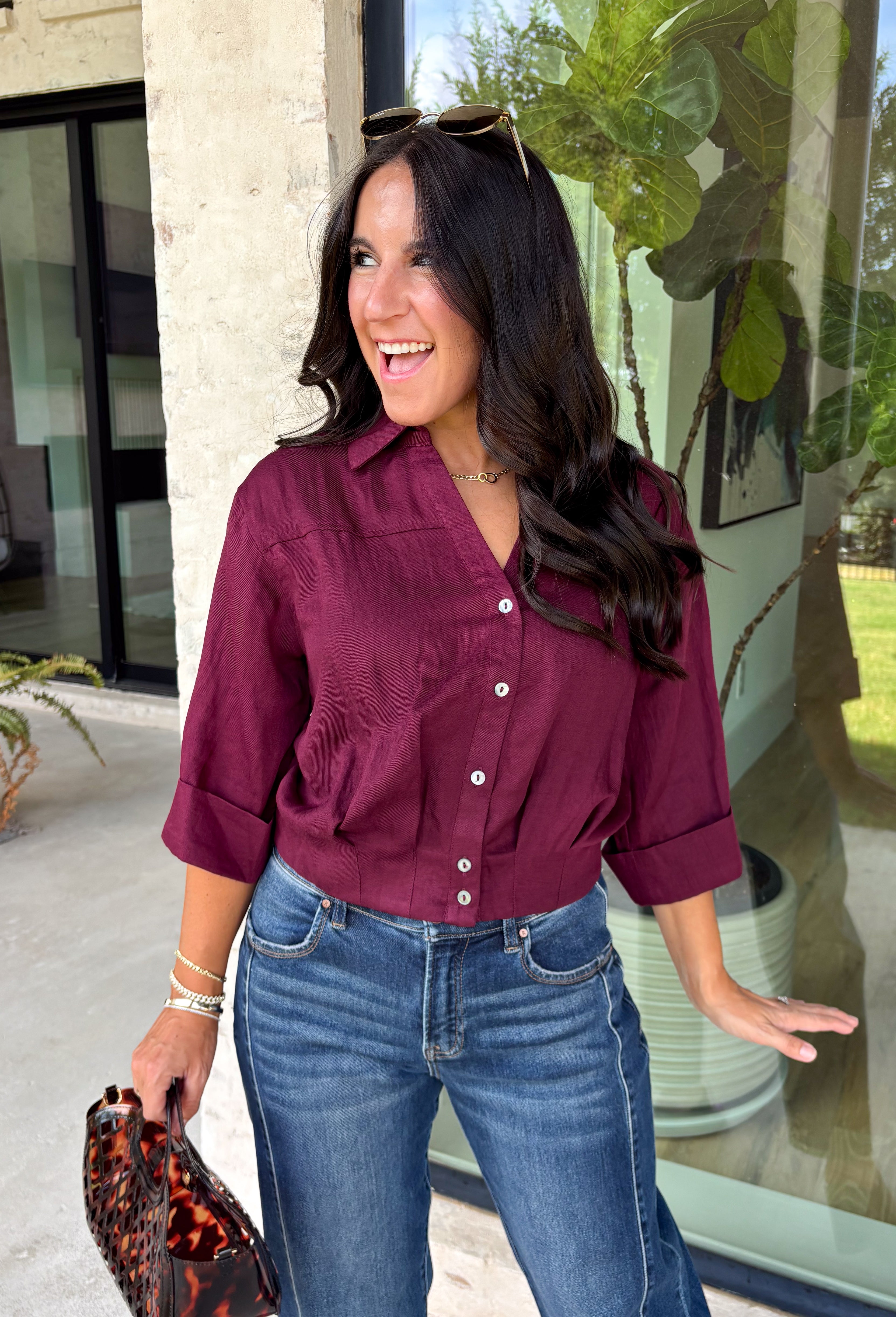 Every wardrobe needs a timeless wine blouse, and this versatile top from Entro is one you'll reach for again and again. Designed with a flattering v-neckline and button-front closure, this effortlessly polished piece transitions seamlessly from workdays to weekends. The ¾ roll-tab sleeves offer versatile styling, while the elasticized smocked back hem creates a comfortable fit with a modern touch. 