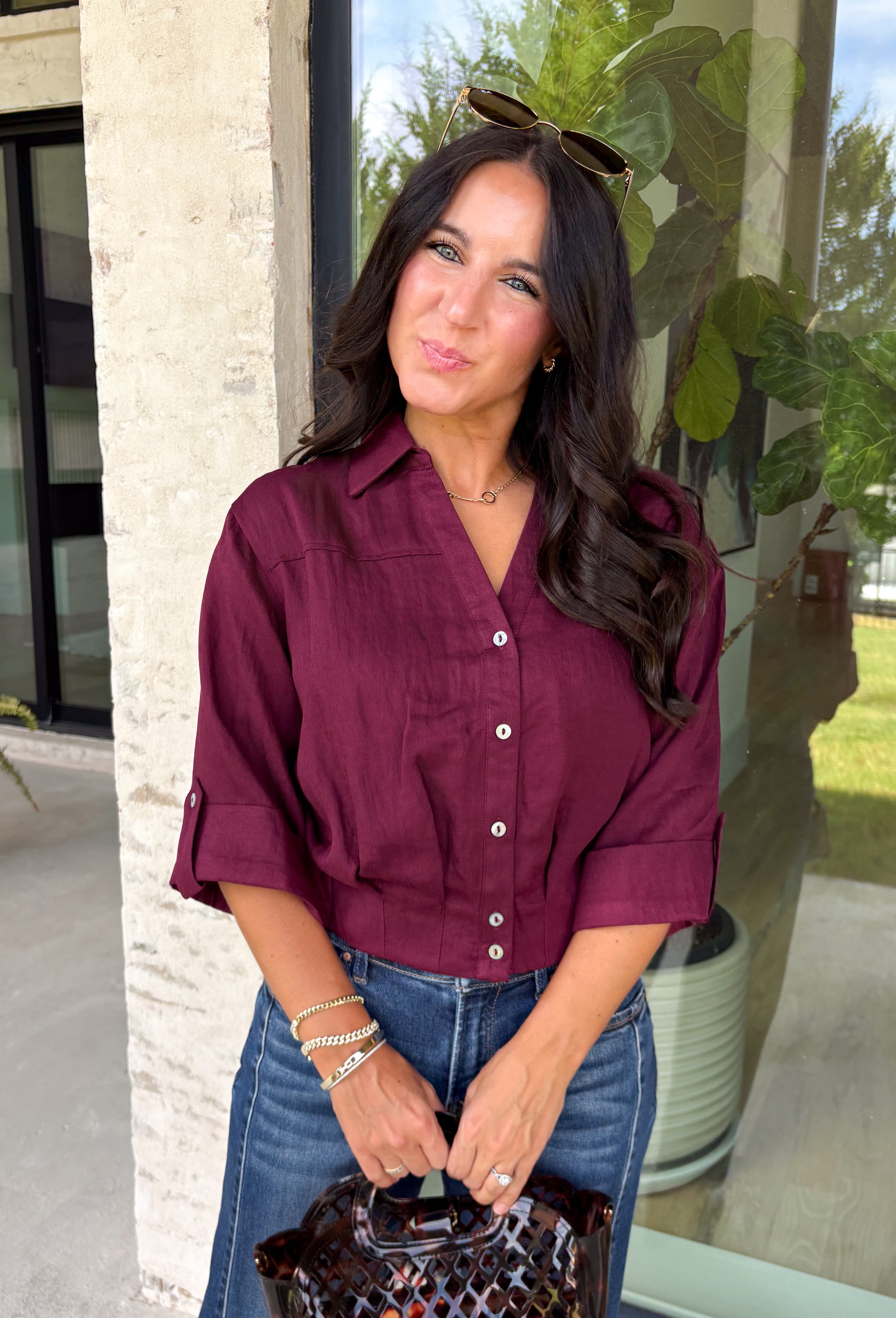 Every wardrobe needs a timeless wine blouse, and this versatile top from Entro is one you'll reach for again and again. Designed with a flattering v-neckline and button-front closure, this effortlessly polished piece transitions seamlessly from workdays to weekends. The ¾ roll-tab sleeves offer versatile styling, while the elasticized smocked back hem creates a comfortable fit with a modern touch. 