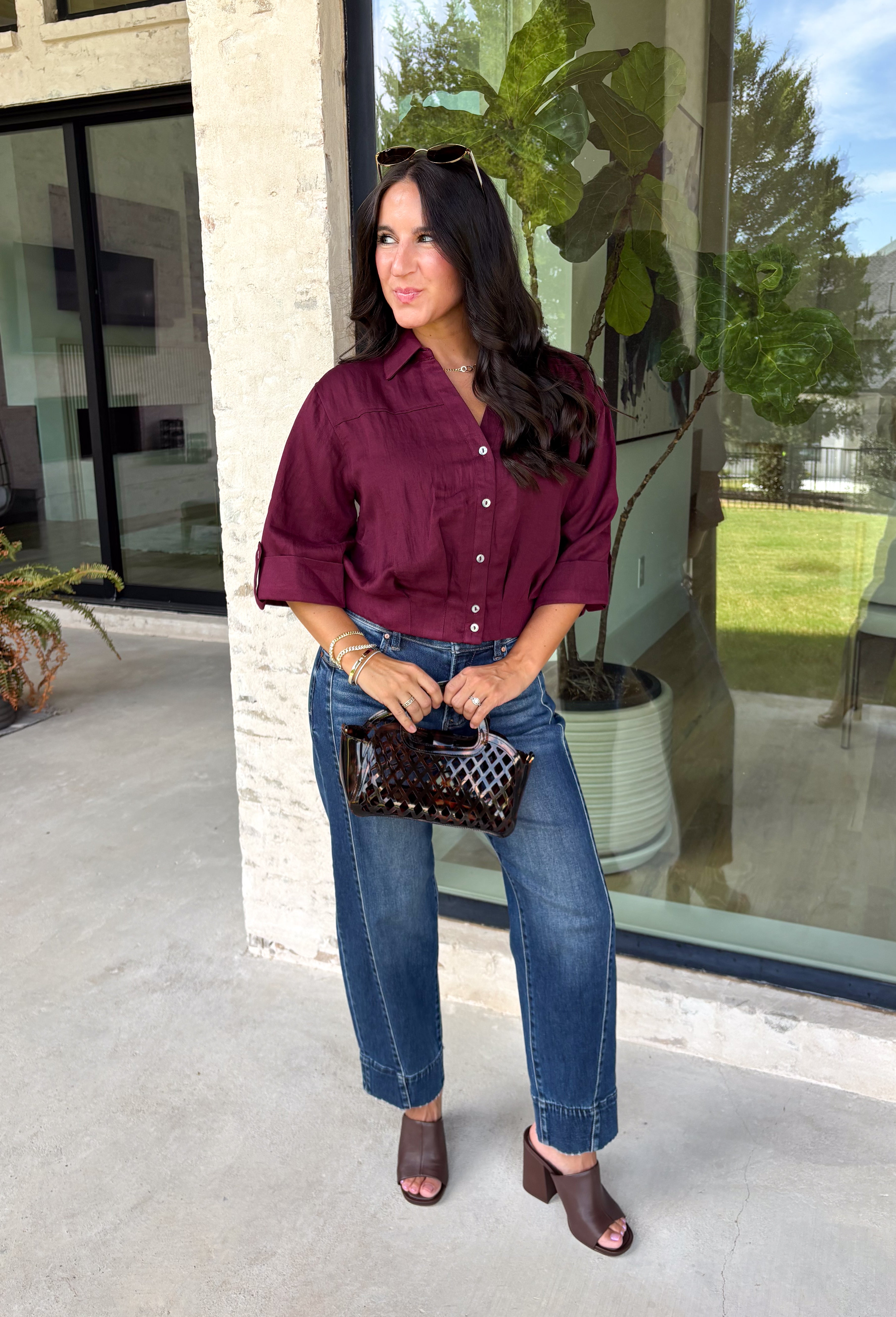 Every wardrobe needs a timeless wine blouse, and this versatile top from Entro is one you'll reach for again and again. Designed with a flattering v-neckline and button-front closure, this effortlessly polished piece transitions seamlessly from workdays to weekends. The ¾ roll-tab sleeves offer versatile styling, while the elasticized smocked back hem creates a comfortable fit with a modern touch. 