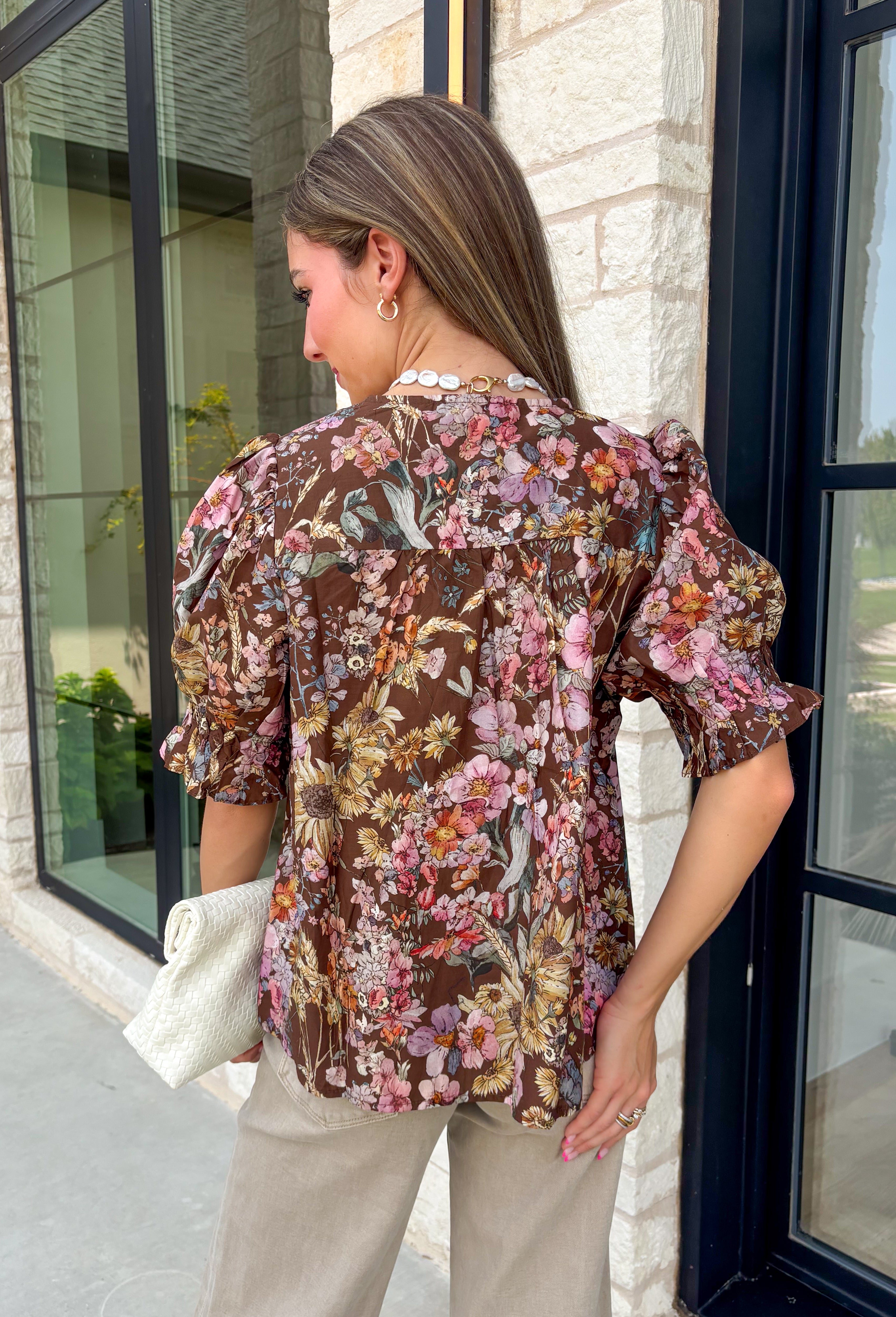 Bring a touch of timeless charm to your fall wardrobe with this beautifully detailed floral blouse. Designed in a warm brown hue with a soft neutral floral print, this top is the perfect blend of feminine and effortless. Delicate pintuck detailing, a flattering v-neckline, and button-front accents create a polished look, while the puff sleeves with smocked ruffle cuffs add just the right amount of romantic flair. 
