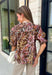 Bring a touch of timeless charm to your fall wardrobe with this beautifully detailed floral blouse. Designed in a warm brown hue with a soft neutral floral print, this top is the perfect blend of feminine and effortless. Delicate pintuck detailing, a flattering v-neckline, and button-front accents create a polished look, while the puff sleeves with smocked ruffle cuffs add just the right amount of romantic flair. 