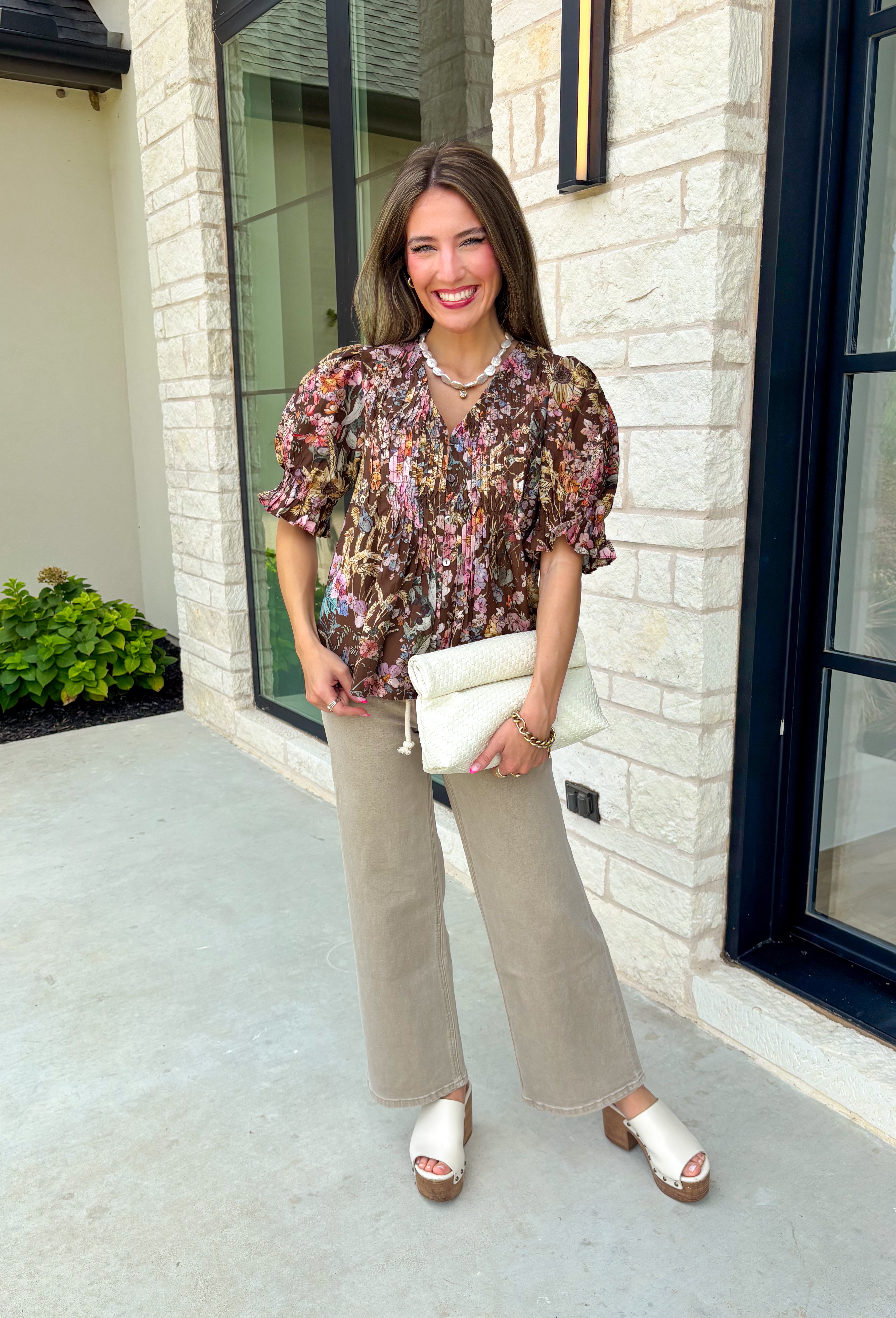 Bring a touch of timeless charm to your fall wardrobe with this beautifully detailed floral blouse. Designed in a warm brown hue with a soft neutral floral print, this top is the perfect blend of feminine and effortless. Delicate pintuck detailing, a flattering v-neckline, and button-front accents create a polished look, while the puff sleeves with smocked ruffle cuffs add just the right amount of romantic flair. 