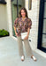 Bring a touch of timeless charm to your fall wardrobe with this beautifully detailed floral blouse. Designed in a warm brown hue with a soft neutral floral print, this top is the perfect blend of feminine and effortless. Delicate pintuck detailing, a flattering v-neckline, and button-front accents create a polished look, while the puff sleeves with smocked ruffle cuffs add just the right amount of romantic flair. 