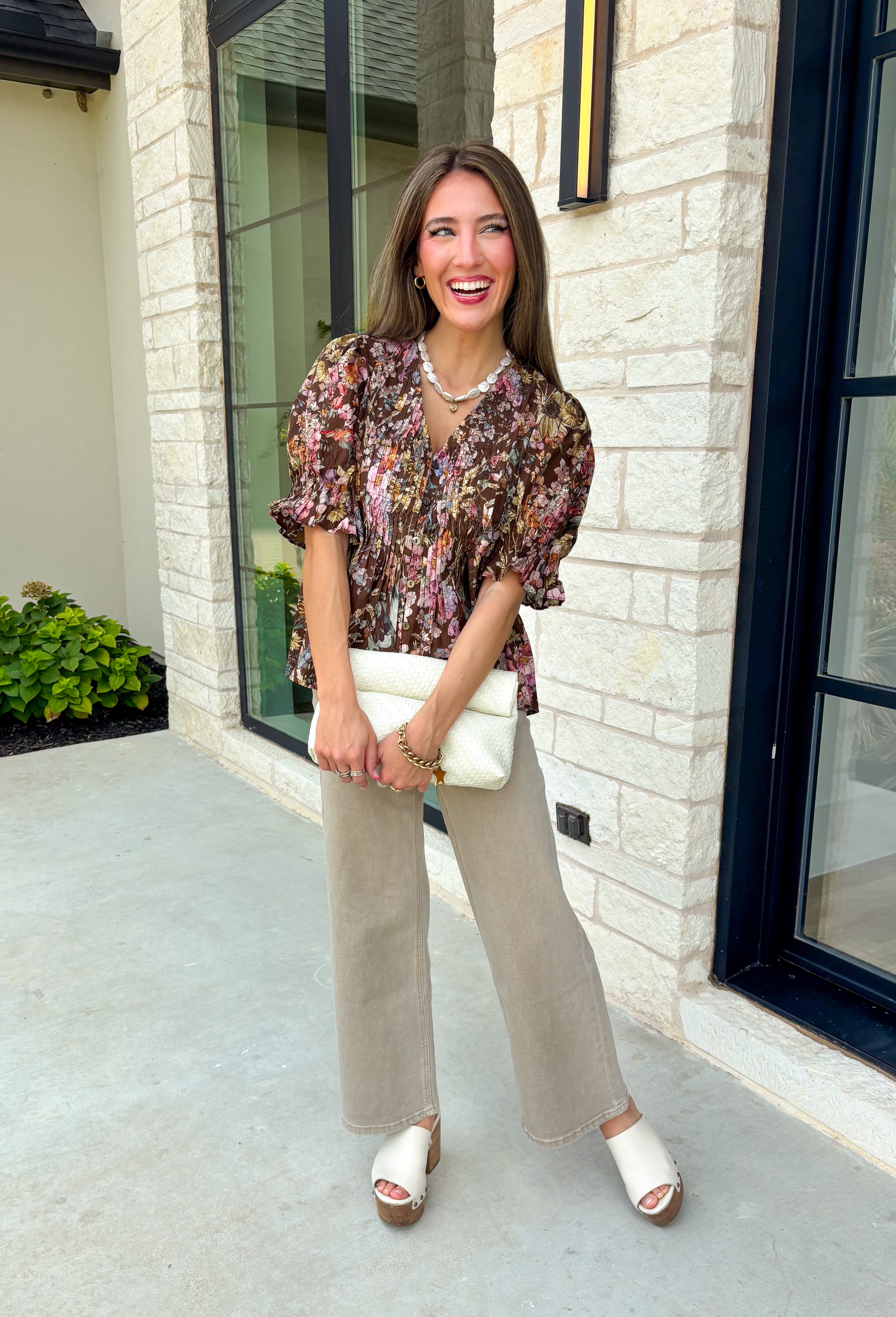 Bring a touch of timeless charm to your fall wardrobe with this beautifully detailed floral blouse. Designed in a warm brown hue with a soft neutral floral print, this top is the perfect blend of feminine and effortless. Delicate pintuck detailing, a flattering v-neckline, and button-front accents create a polished look, while the puff sleeves with smocked ruffle cuffs add just the right amount of romantic flair. 