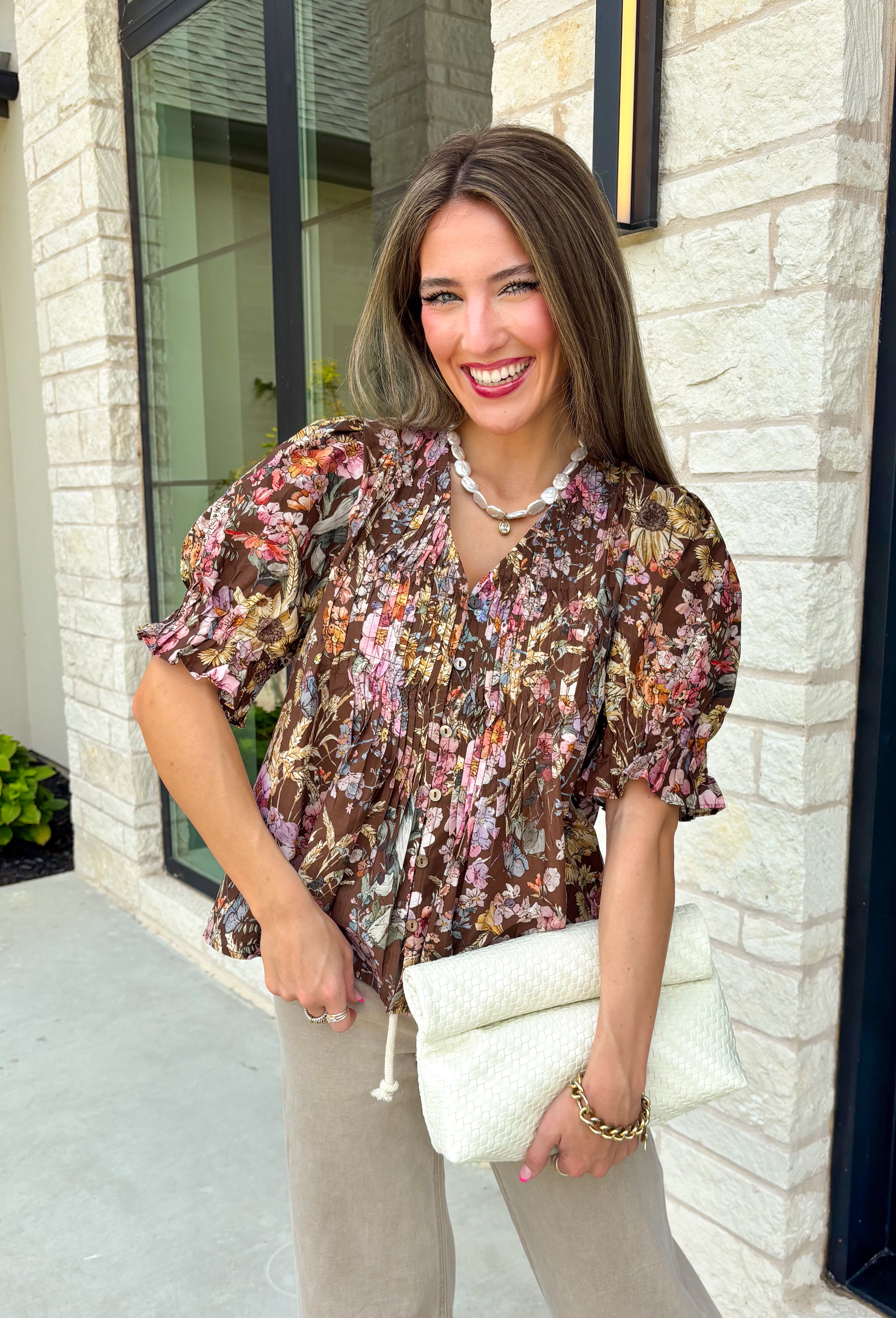 Bring a touch of timeless charm to your fall wardrobe with this beautifully detailed floral blouse. Designed in a warm brown hue with a soft neutral floral print, this top is the perfect blend of feminine and effortless. Delicate pintuck detailing, a flattering v-neckline, and button-front accents create a polished look, while the puff sleeves with smocked ruffle cuffs add just the right amount of romantic flair. 