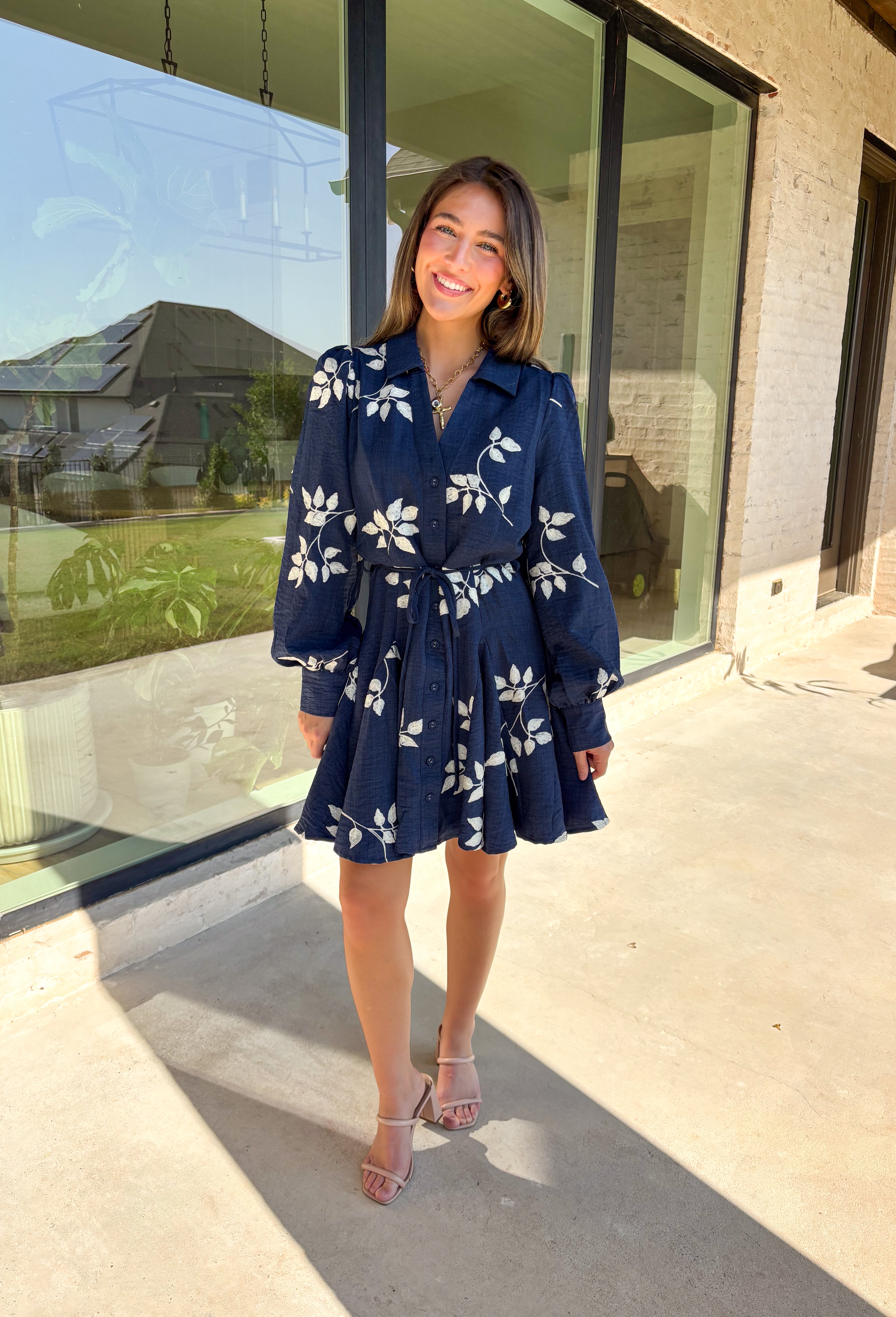 Delicate details and a flowy fit make this navy dress a true fall favorite. Embroidered with an off-white leaf print throughout, it strikes the perfect balance of playful and polished. The collared neckline and button-down front add structure, while the self-tie waist flatters your shape. Finished with buttoned cuffs and a flowy skirt, this fully lined dress is both comfortable and chic—ready for anything from weekday wear to seasonal celebrations.