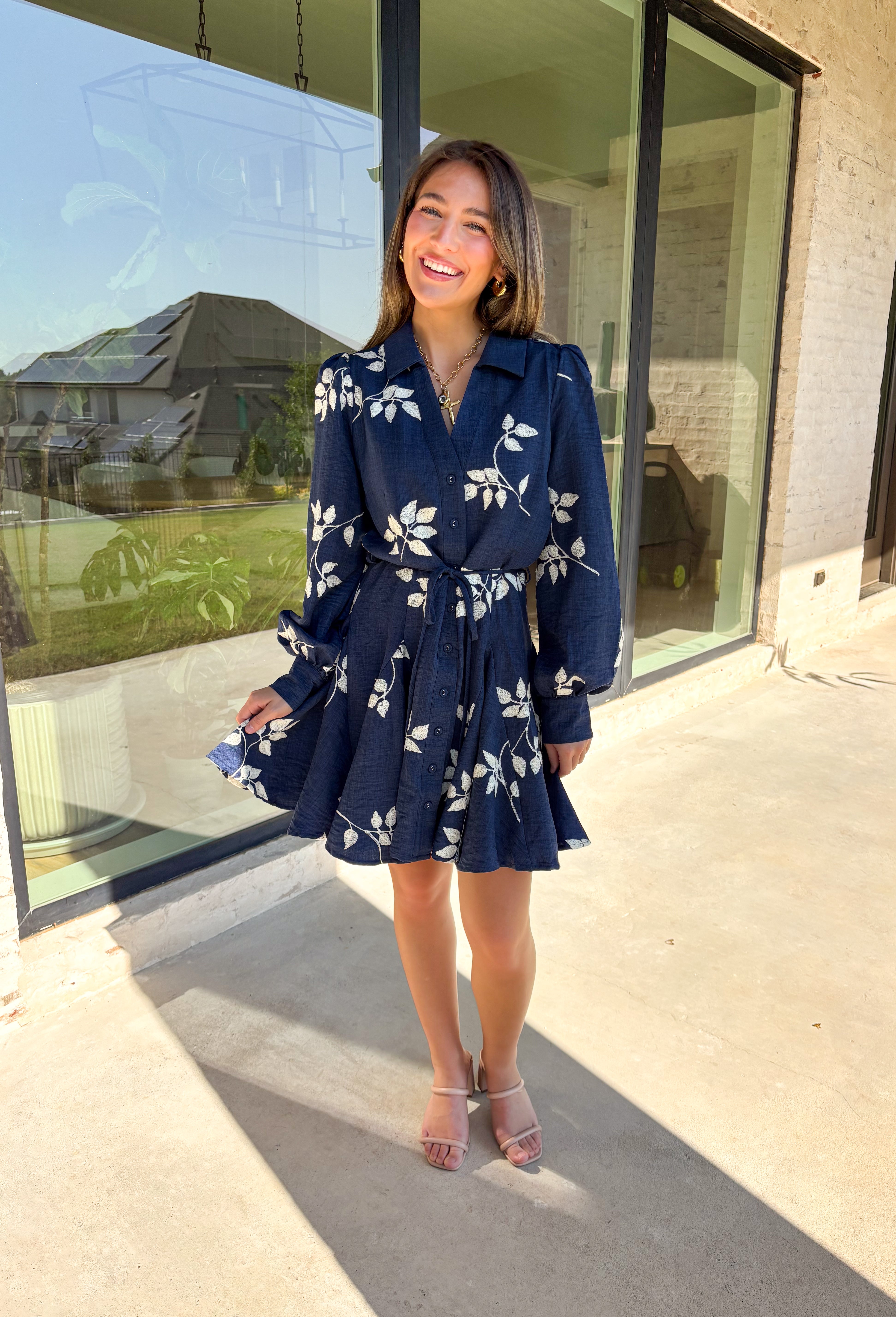 Delicate details and a flowy fit make this navy dress a true fall favorite. Embroidered with an off-white leaf print throughout, it strikes the perfect balance of playful and polished. The collared neckline and button-down front add structure, while the self-tie waist flatters your shape. Finished with buttoned cuffs and a flowy skirt, this fully lined dress is both comfortable and chic—ready for anything from weekday wear to seasonal celebrations.