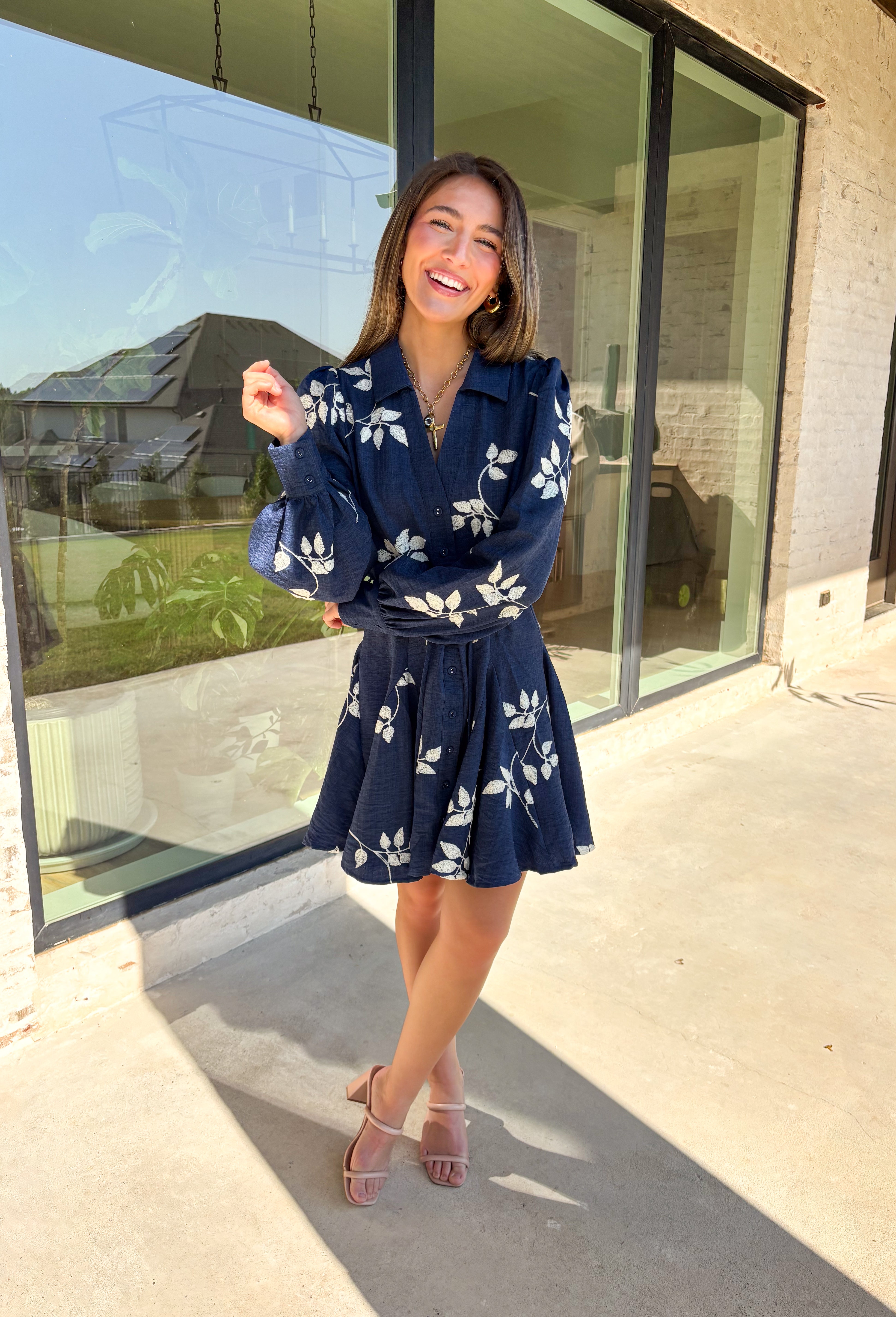 Delicate details and a flowy fit make this navy dress a true fall favorite. Embroidered with an off-white leaf print throughout, it strikes the perfect balance of playful and polished. The collared neckline and button-down front add structure, while the self-tie waist flatters your shape. Finished with buttoned cuffs and a flowy skirt, this fully lined dress is both comfortable and chic—ready for anything from weekday wear to seasonal celebrations.