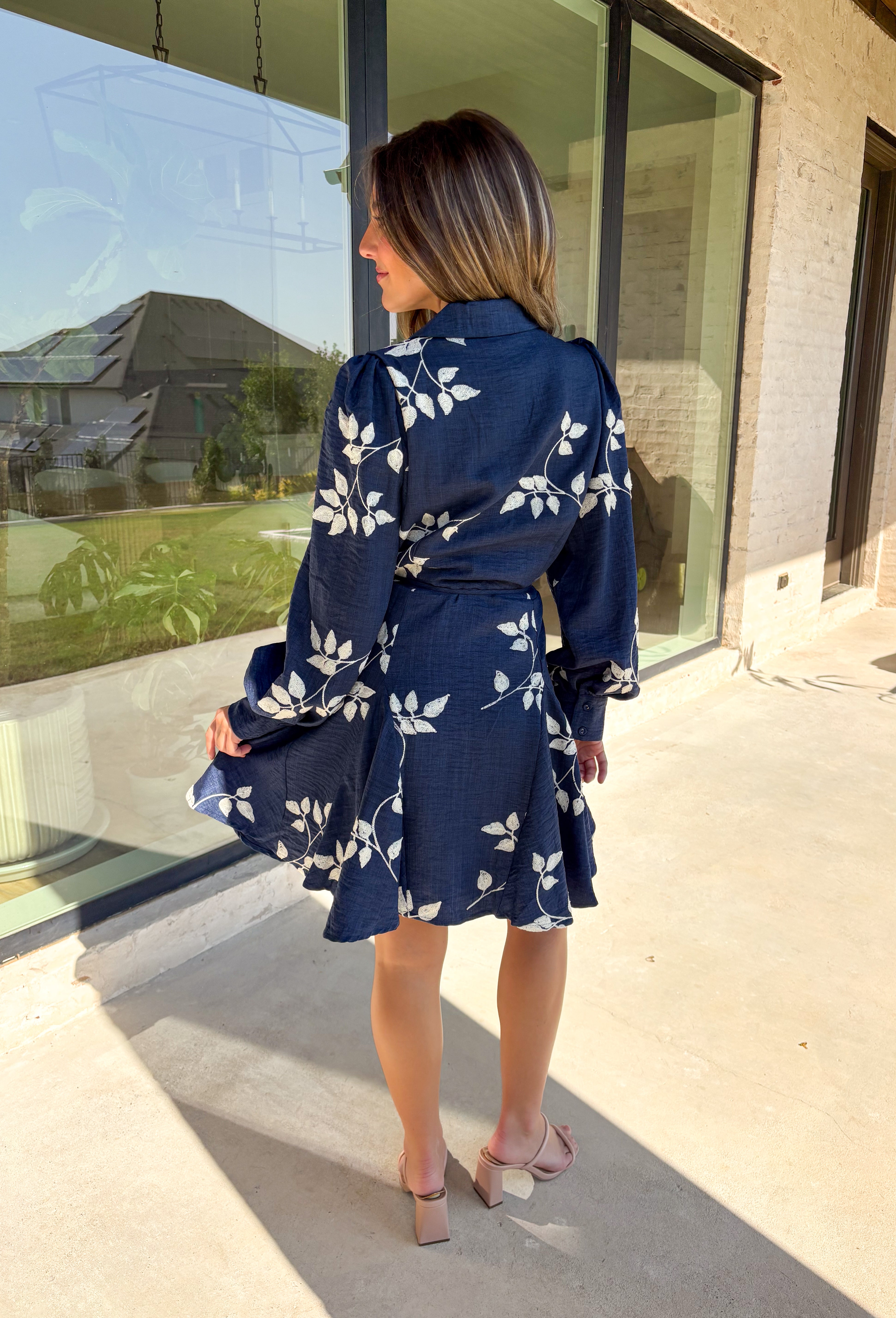 Delicate details and a flowy fit make this navy dress a true fall favorite. Embroidered with an off-white leaf print throughout, it strikes the perfect balance of playful and polished. The collared neckline and button-down front add structure, while the self-tie waist flatters your shape. Finished with buttoned cuffs and a flowy skirt, this fully lined dress is both comfortable and chic—ready for anything from weekday wear to seasonal celebrations.