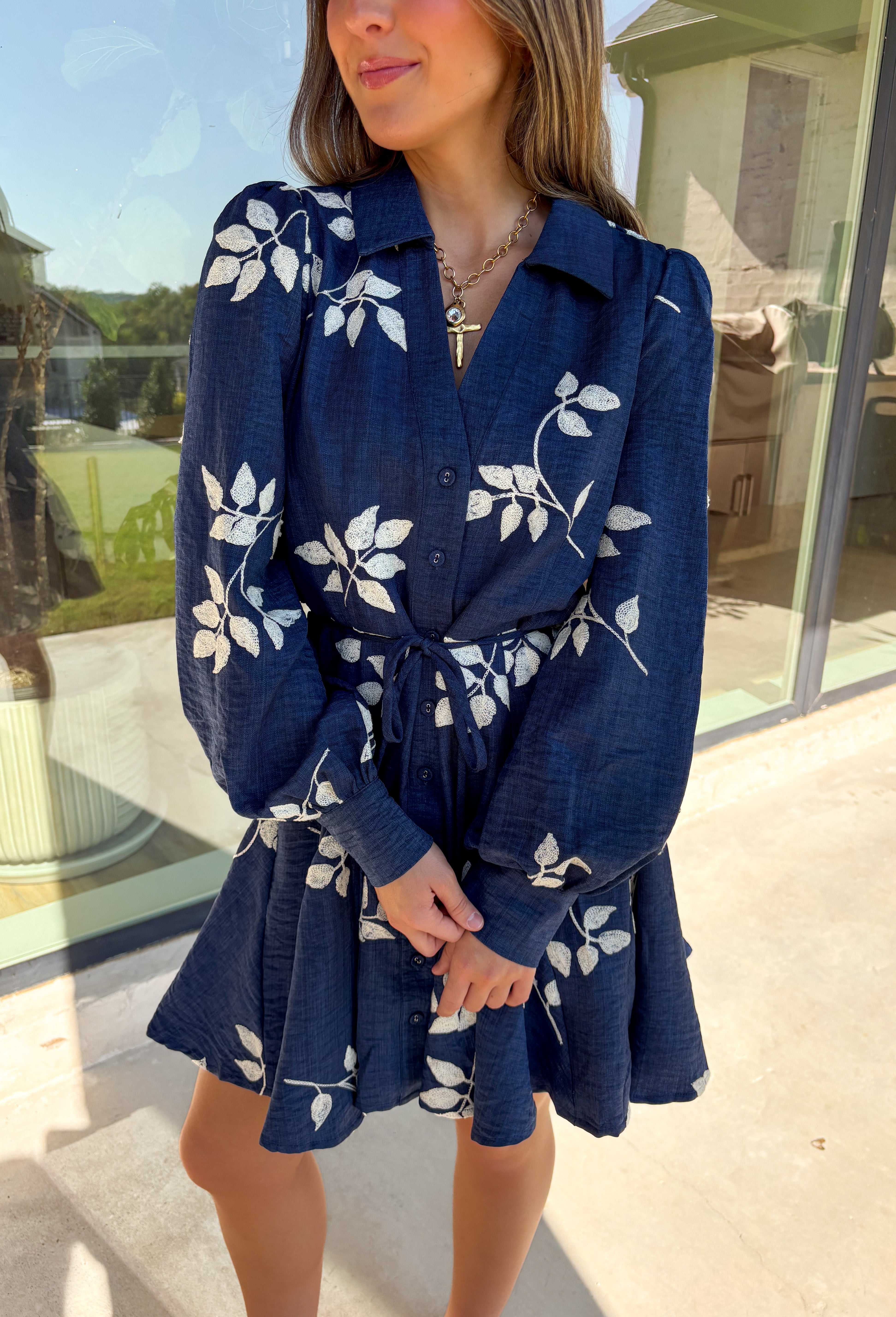 Delicate details and a flowy fit make this navy dress a true fall favorite. Embroidered with an off-white leaf print throughout, it strikes the perfect balance of playful and polished. The collared neckline and button-down front add structure, while the self-tie waist flatters your shape. Finished with buttoned cuffs and a flowy skirt, this fully lined dress is both comfortable and chic—ready for anything from weekday wear to seasonal celebrations.