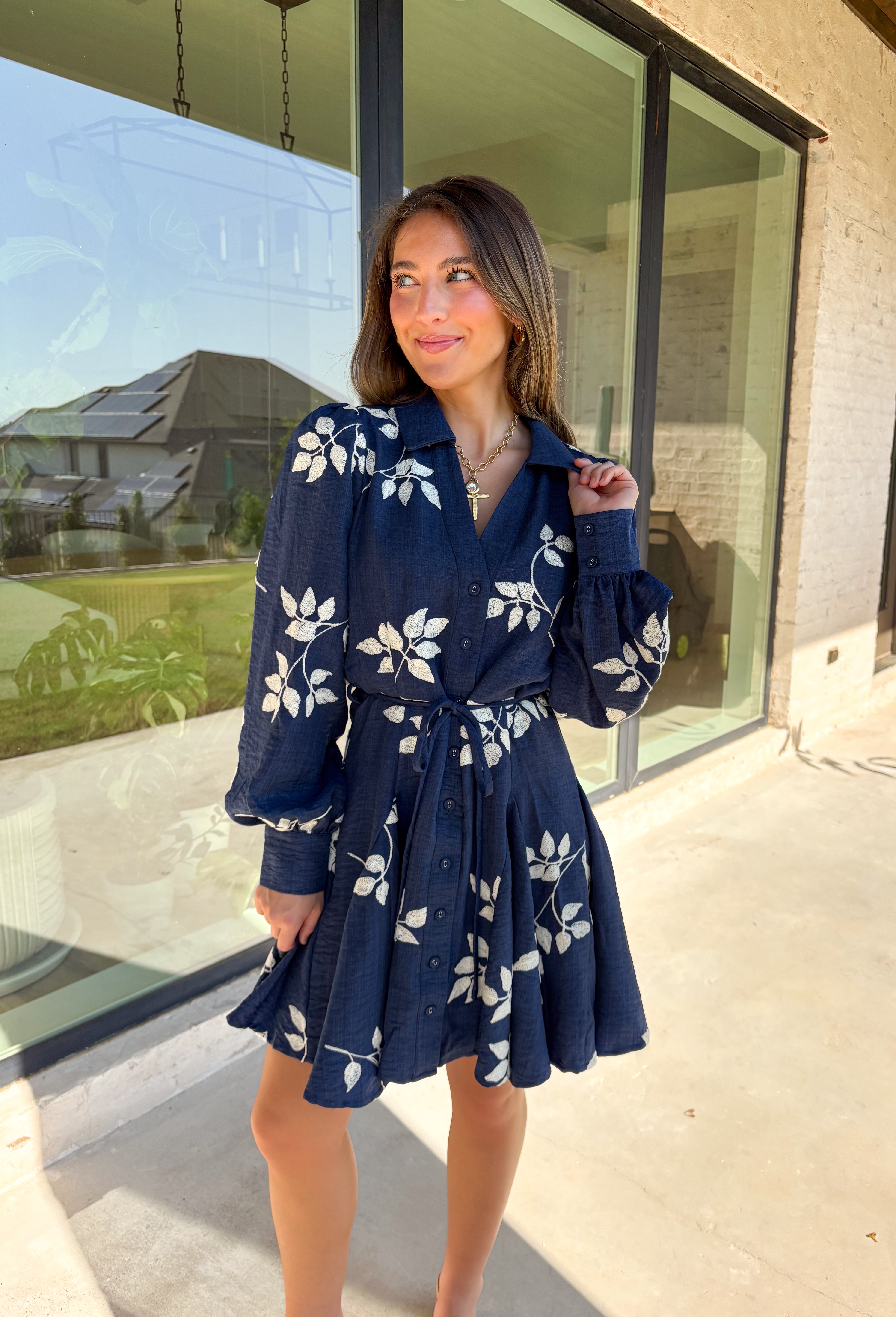 Delicate details and a flowy fit make this navy dress a true fall favorite. Embroidered with an off-white leaf print throughout, it strikes the perfect balance of playful and polished. The collared neckline and button-down front add structure, while the self-tie waist flatters your shape. Finished with buttoned cuffs and a flowy skirt, this fully lined dress is both comfortable and chic—ready for anything from weekday wear to seasonal celebrations.