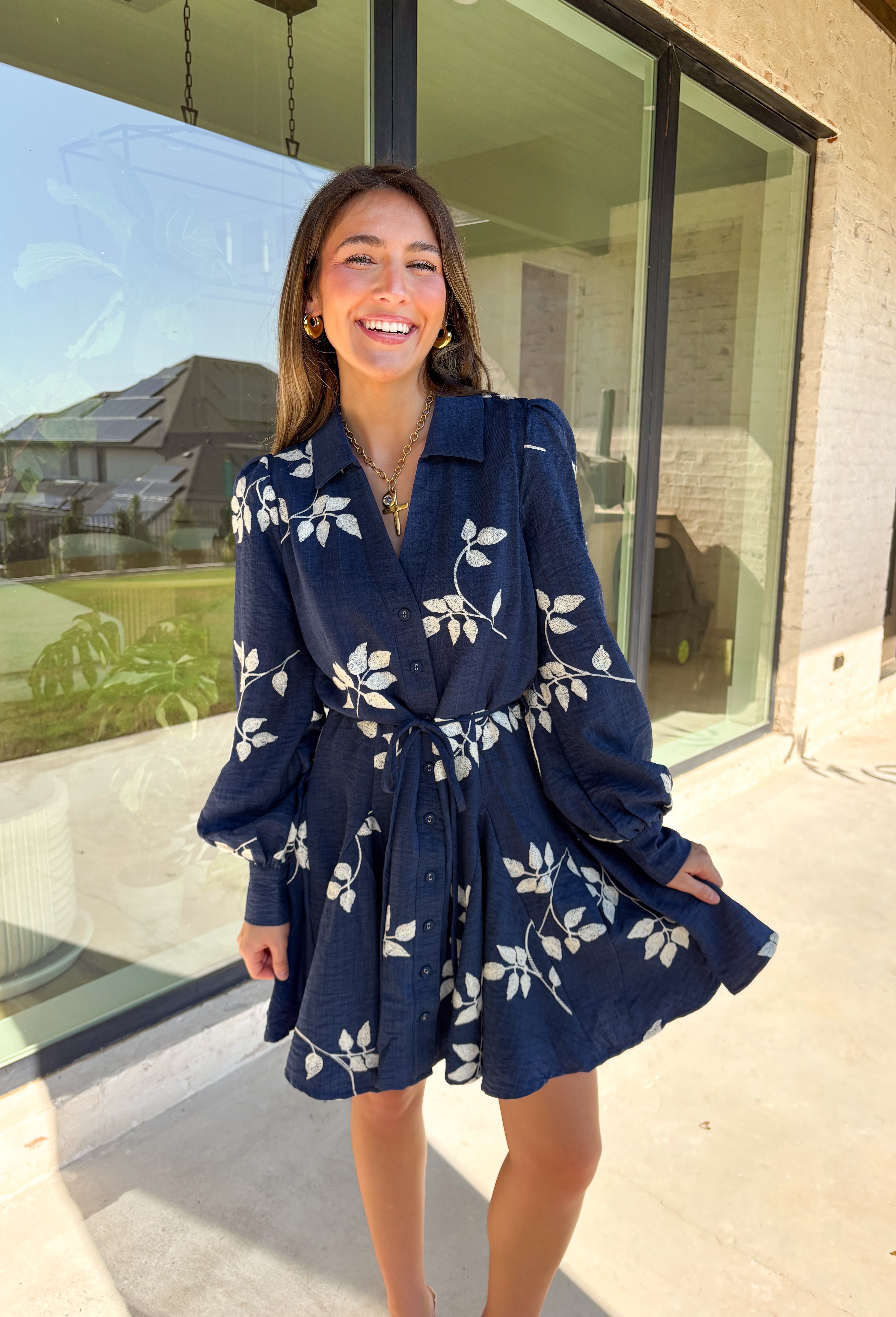 Delicate details and a flowy fit make this navy dress a true fall favorite. Embroidered with an off-white leaf print throughout, it strikes the perfect balance of playful and polished. The collared neckline and button-down front add structure, while the self-tie waist flatters your shape. Finished with buttoned cuffs and a flowy skirt, this fully lined dress is both comfortable and chic—ready for anything from weekday wear to seasonal celebrations.