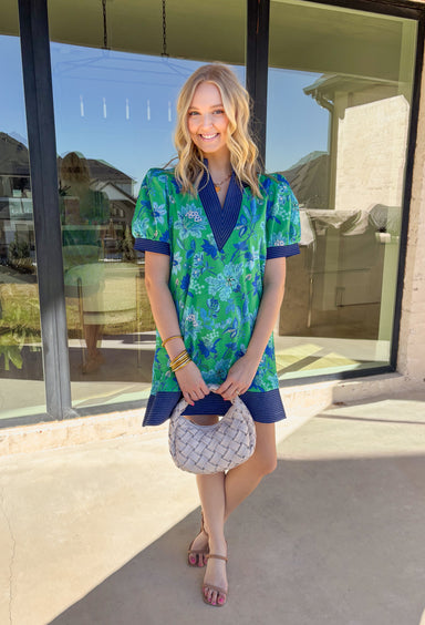 Fresh, easy, and perfect for sunny spring days, this green short sleeve dress by Entro is a go-to you’ll love wearing on repeat. Featuring a blue floral print, it feels light and cheerful for the season. Navy stitch accent contrast band details add a touch of structure, while side pockets bring everyday practicality. Fully lined and made from breathable cotton, this lightweight dress is comfortable, flattering, and effortlessly wearable.