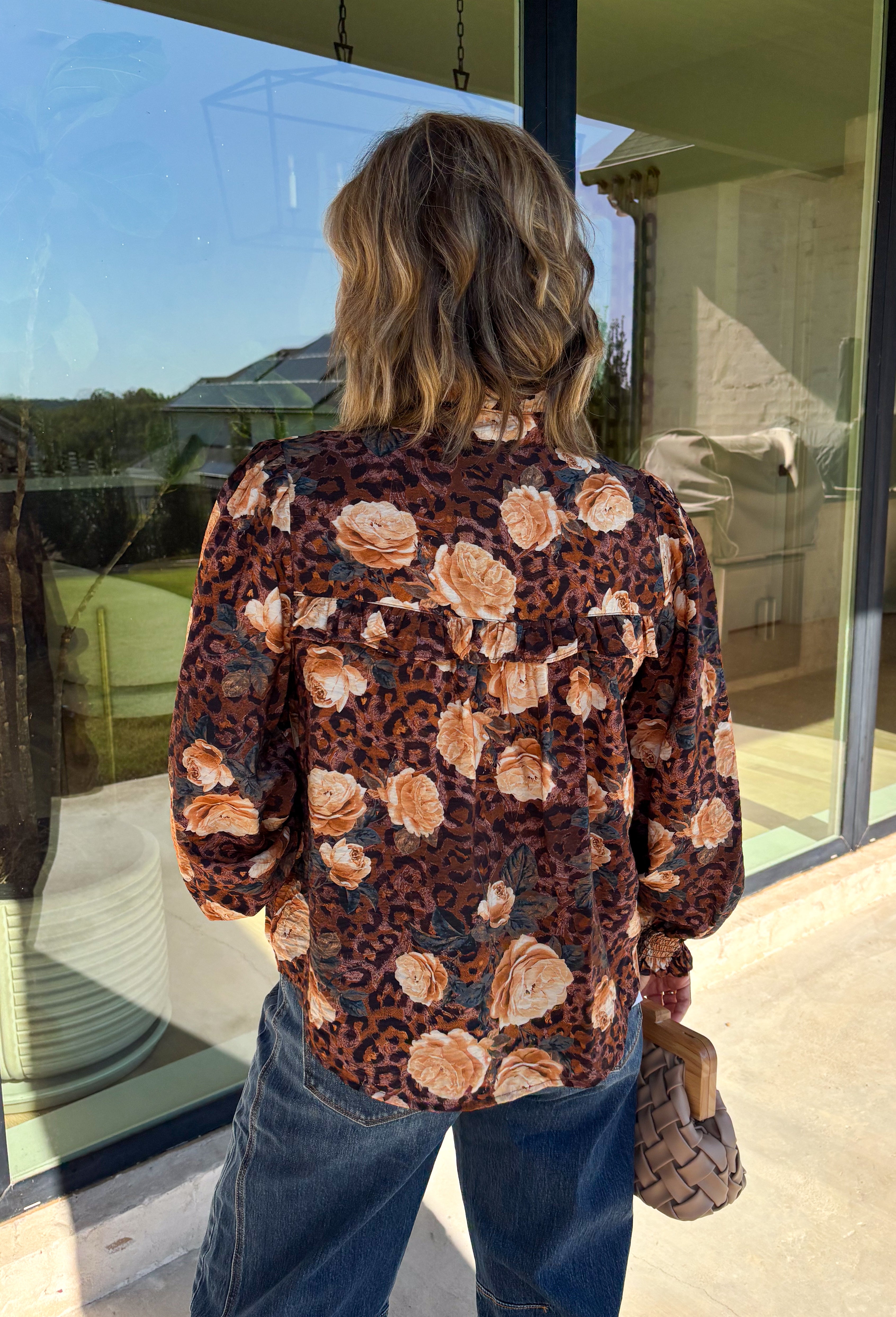 Bring a fresh twist to your fall wardrobe with this beautifully detailed blouse from Fate. Featuring a rich brown leopard-inspired print accented with a soft neutral floral design, this feminine top effortlessly blends bold style with timeless charm. The button-front silhouette is finished with a subtle ruffle neckline and delicate ruffle details throughout the front and back for added texture. 
